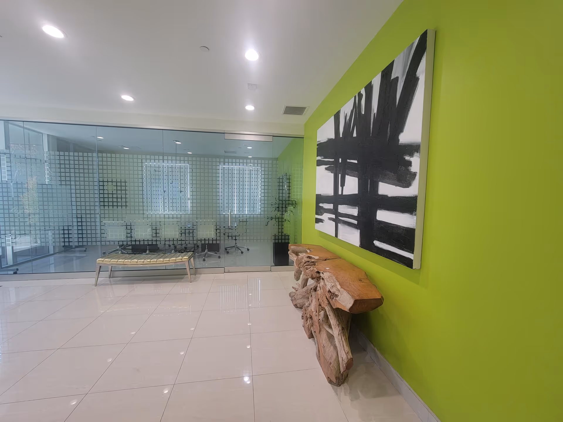 Bright modern lobby featuring a lime-green wall, glass-walled meeting room, and abstract painting.