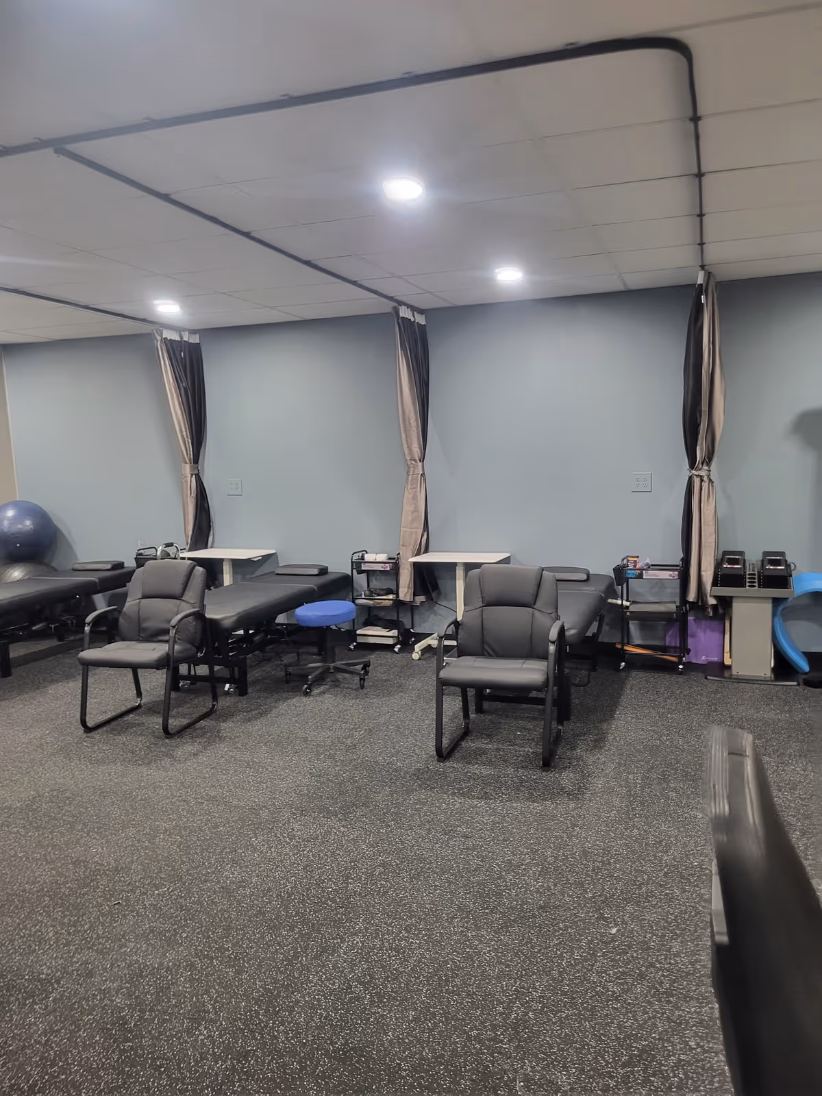 Interior therapy room with chairs, curtained treatment bays, and equipment along blue walls.
