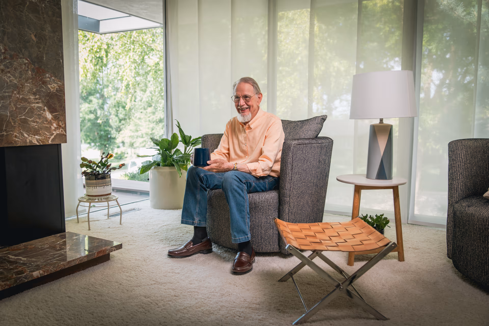 An elderly man sits in a modern senior living lounge with plants and a floor lamp.