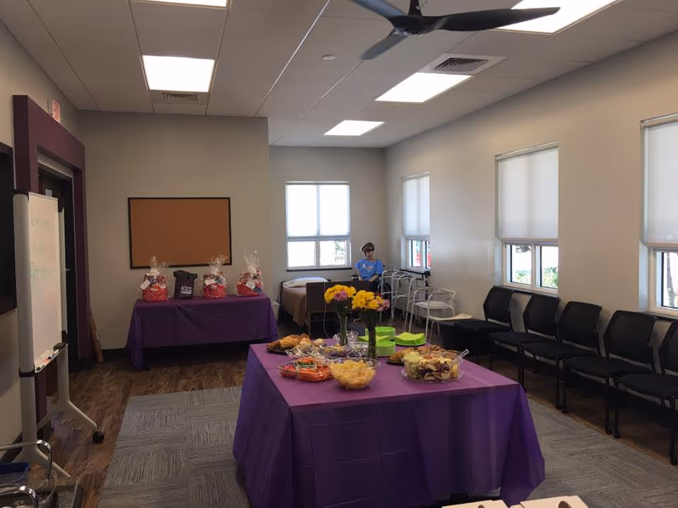 Multipurpose interior with purple tablecloths, snacks, and a staff member near windows.