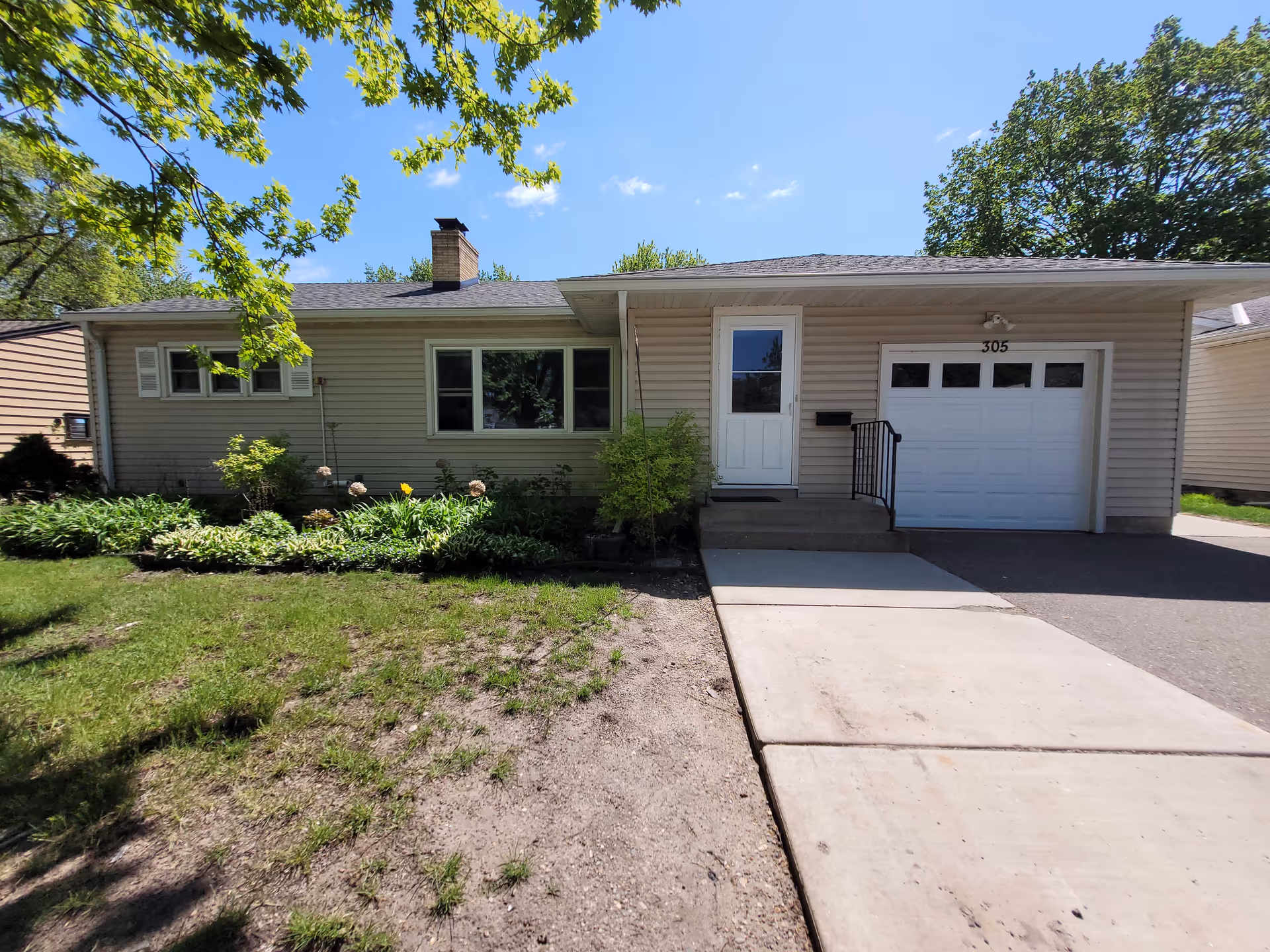 Single-story beige house with front door, attached garage, and landscaped yard.