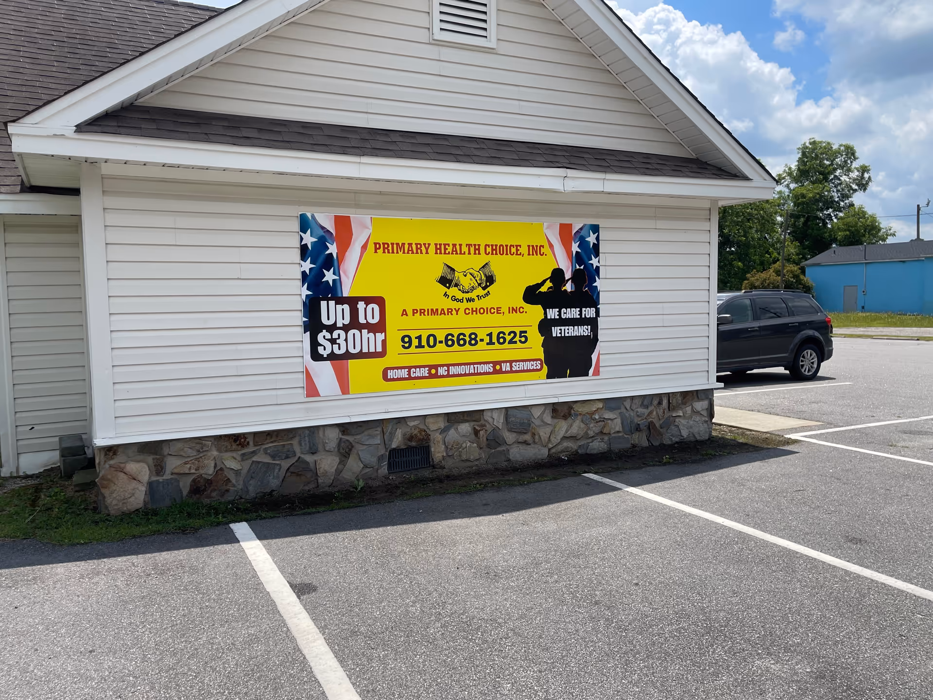 White building with stone foundation and patriotic banner, parking lot, and SUV
