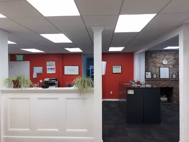 Lobby reception area with white counter, red walls, plants, and brick accent wall.