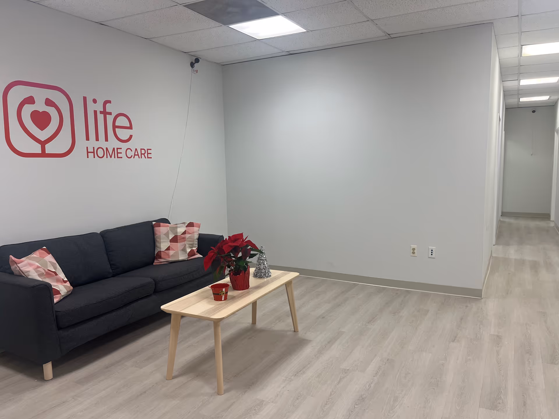 Sitting area with gray couch, coffee table, holiday decor, and Life Home Care logo on wall.
