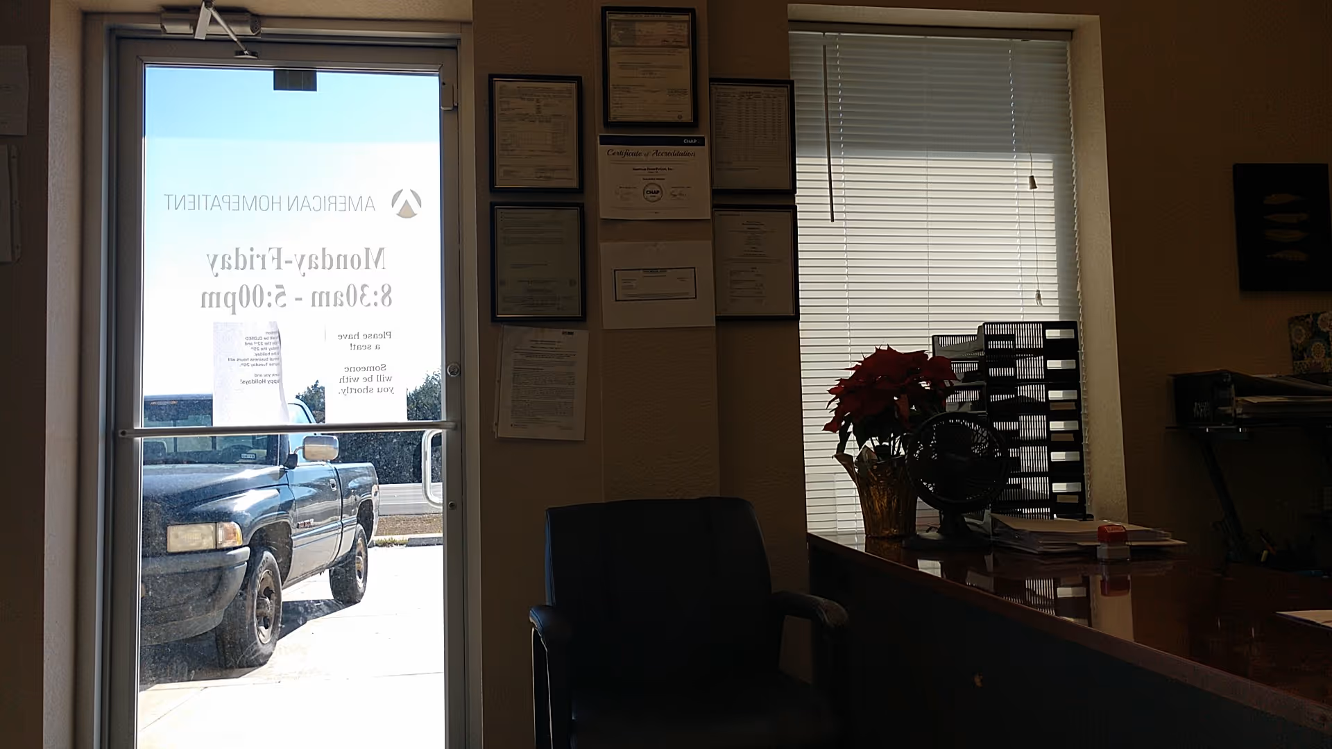 Interior office area with desk, blinds, certificates, a plant, and a view of the outside truck.