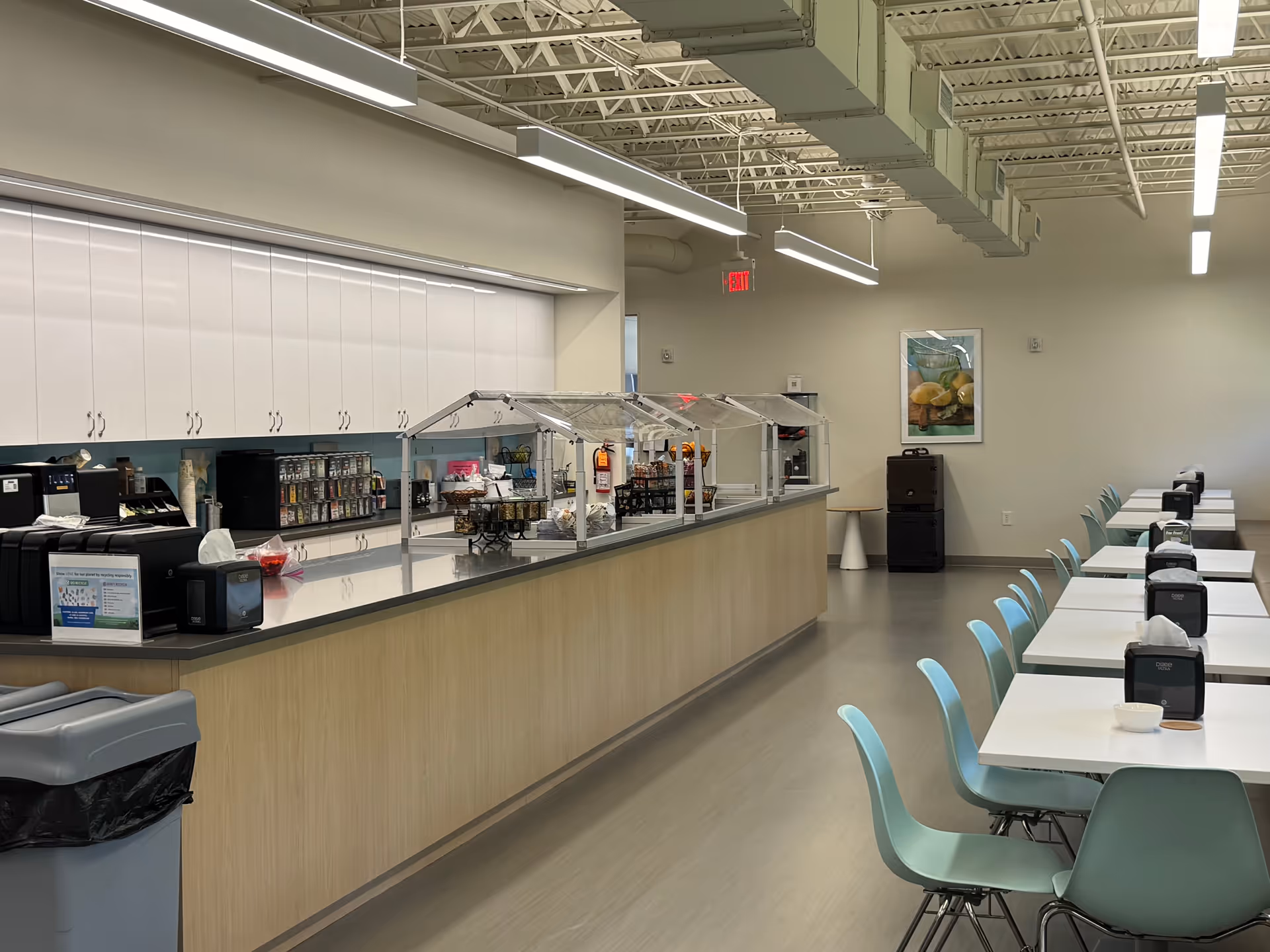 Long dining area with serving counter and row of light blue chairs facing white tables.