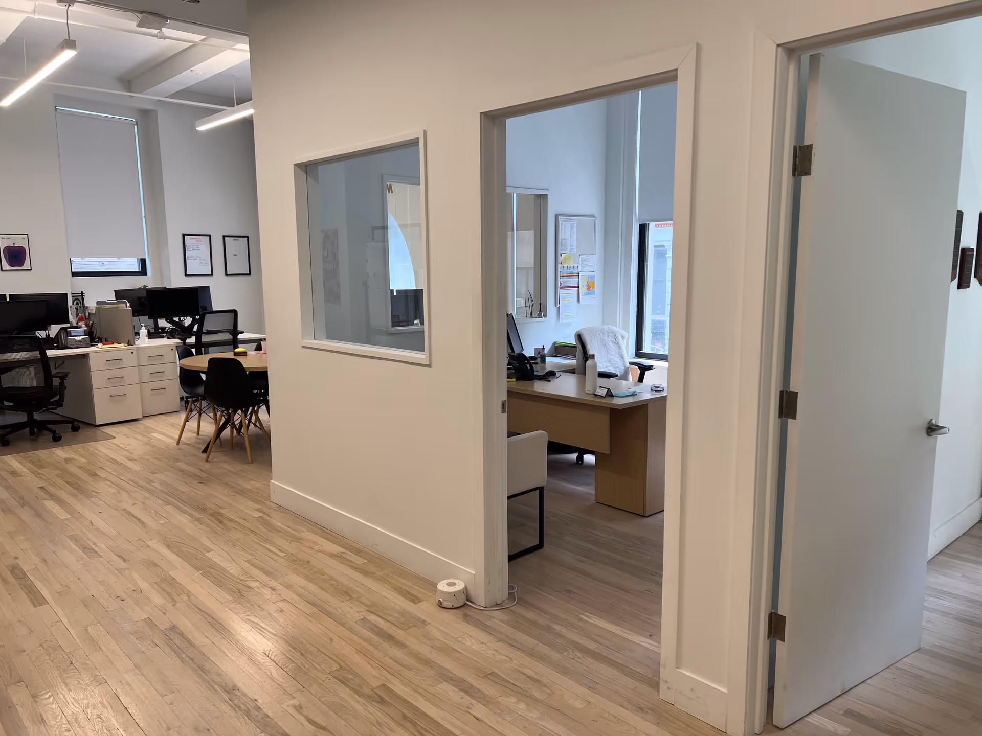 Open interior office area with desks, chairs and glass-walled private rooms.