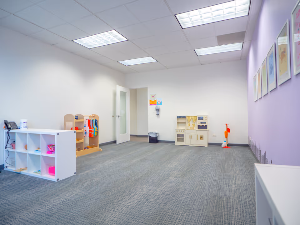 Child-friendly play area with toy shelves, mini kitchen, and purple accent wall.