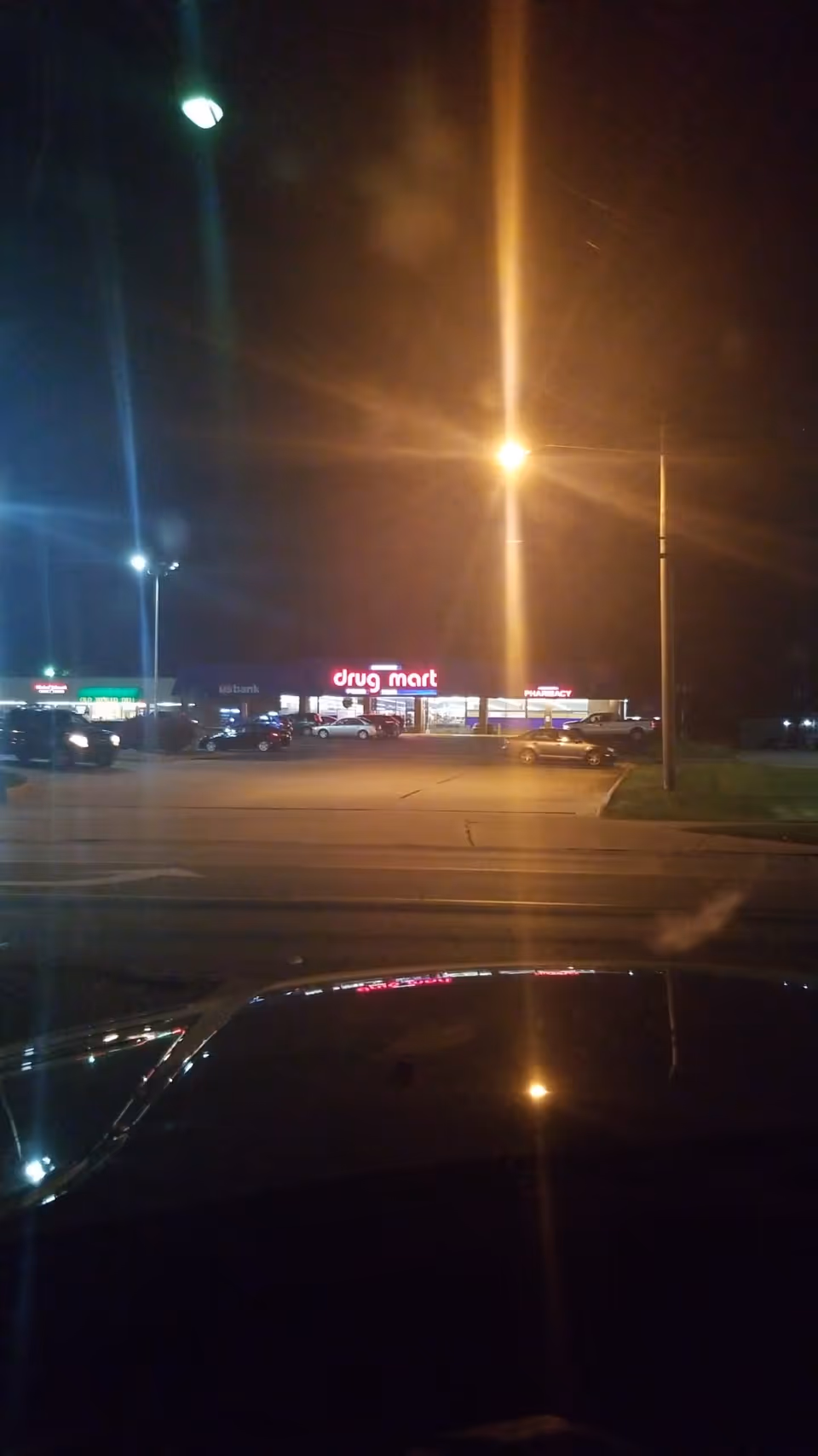Nighttime exterior view of a Discount Drug Mart storefront in a parking lot.