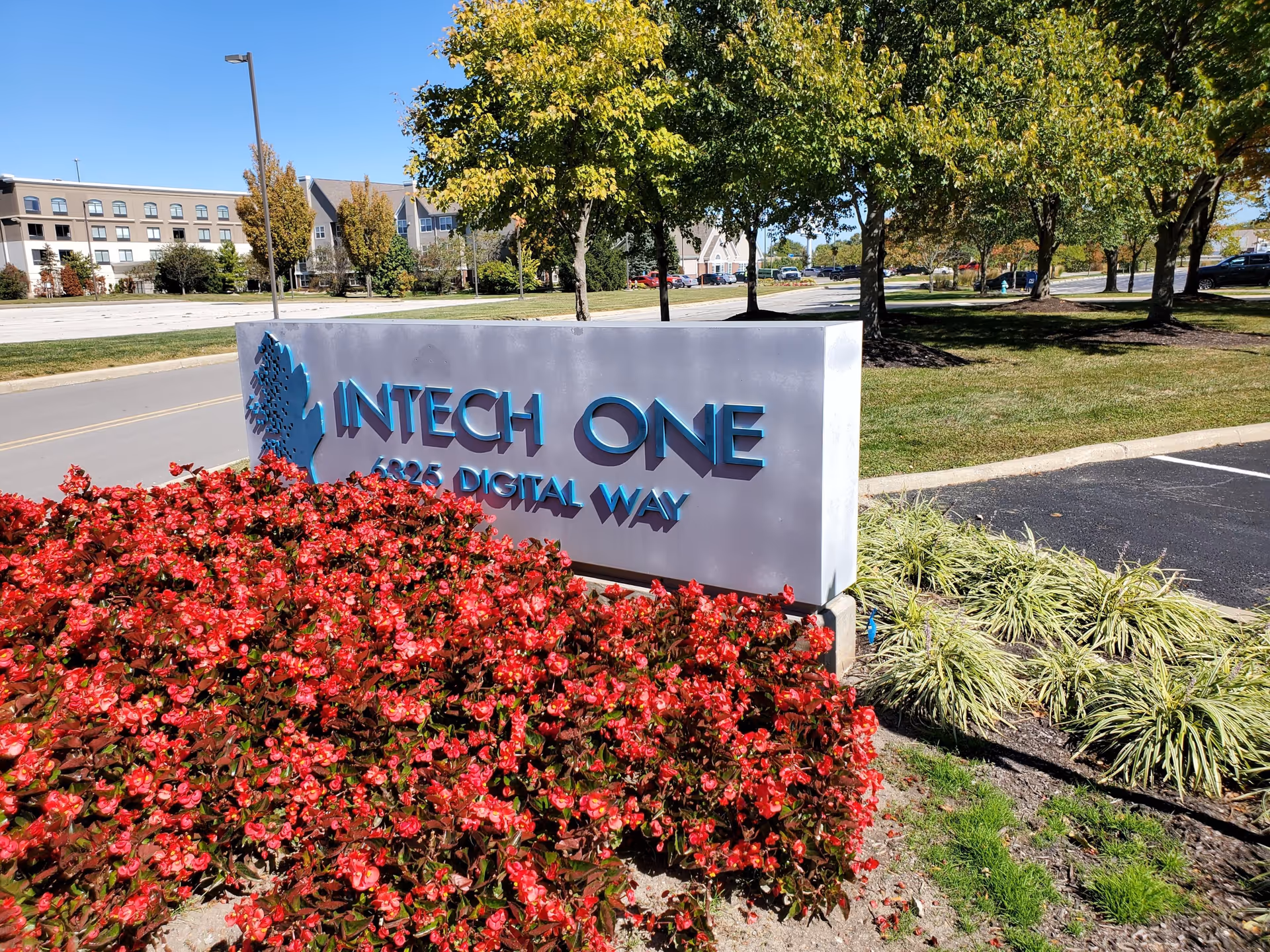 A large concrete sign reading INTECH ONE sits among red flowers and trees.