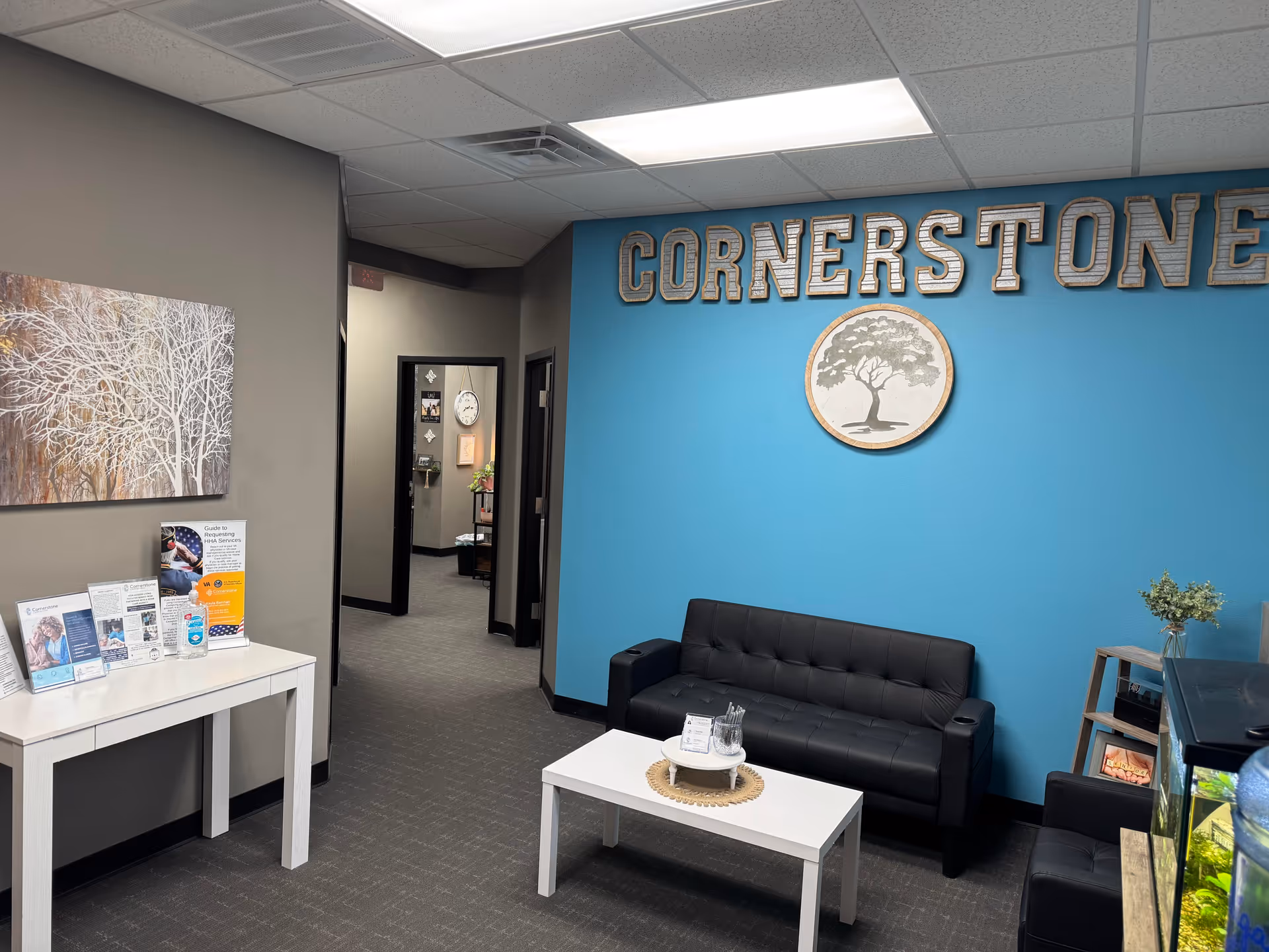 Reception lobby with blue wall, Cornerstone sign, seating, coffee table, and hallway.