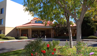 Exterior view of a senior living facility entrance with trees and flowers.
