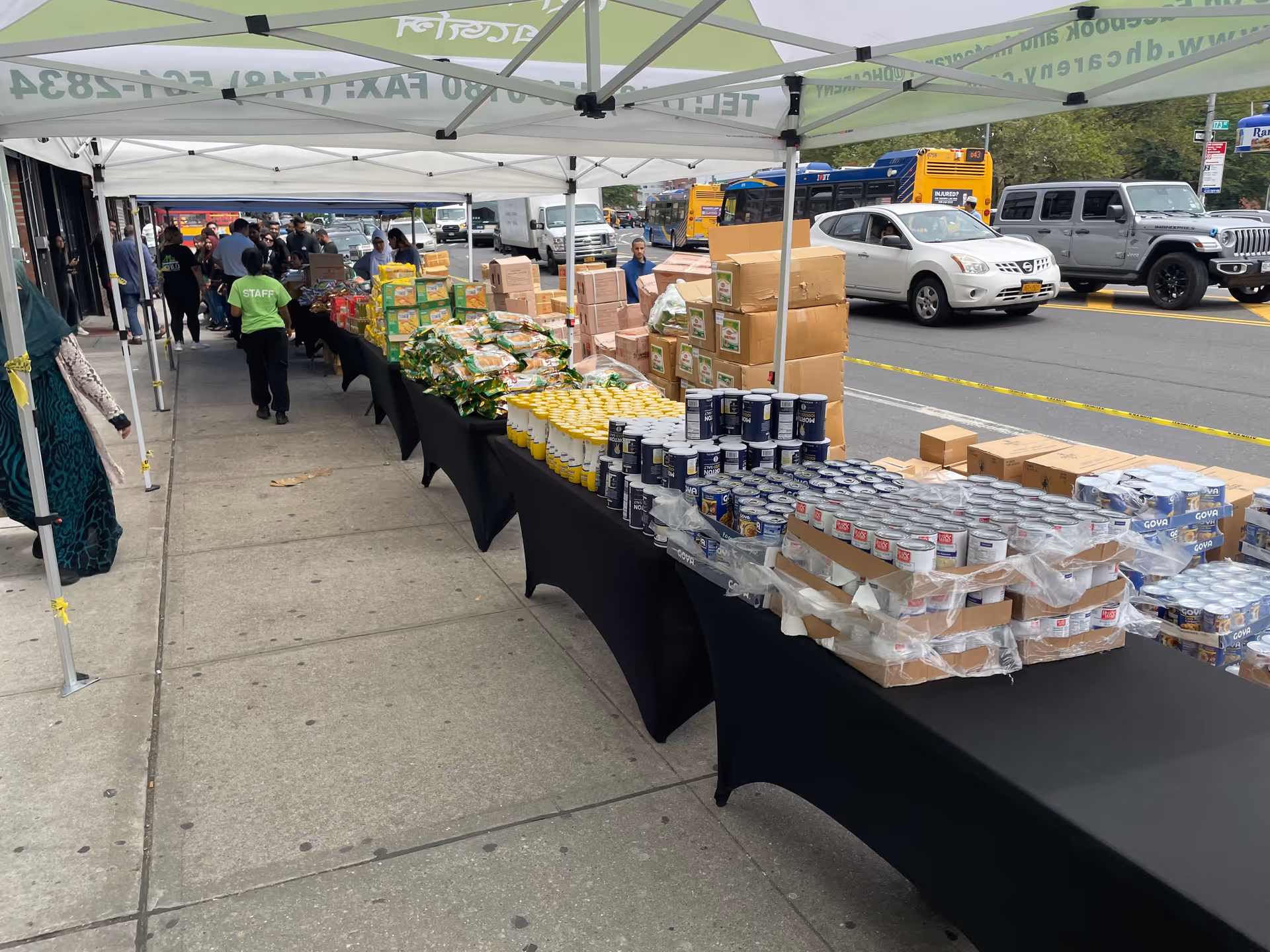 Outdoor street market setup with tents and tables of canned goods and supplies.