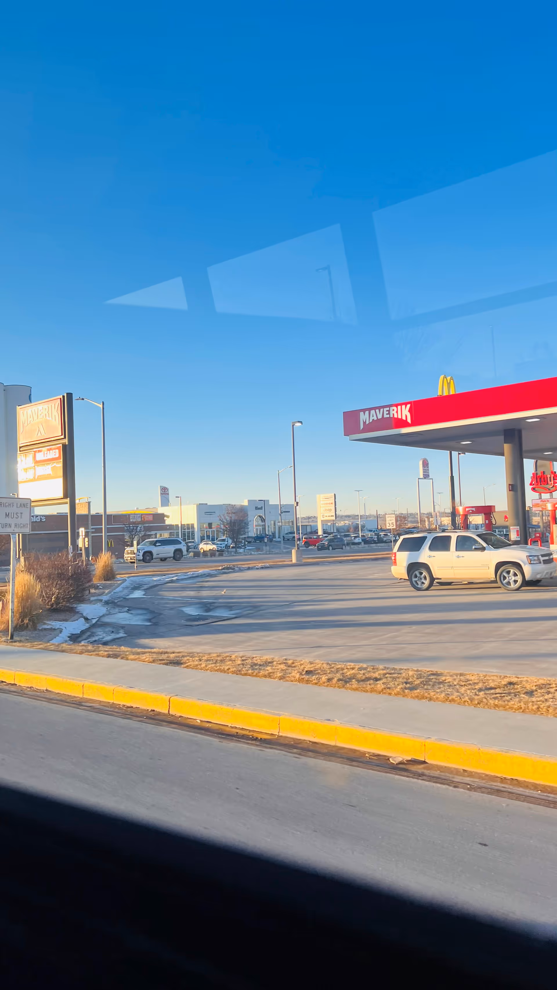 Outdoor street view of a Maverik gas station with cars and nearby storefronts.