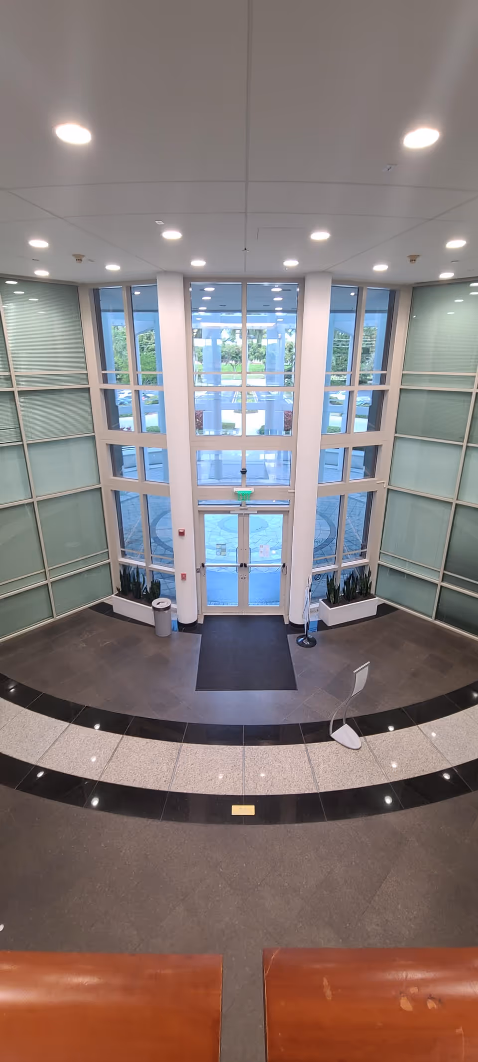 Wide glass-walled lobby with double doors, circular black-and-white tiled floor, and benches.