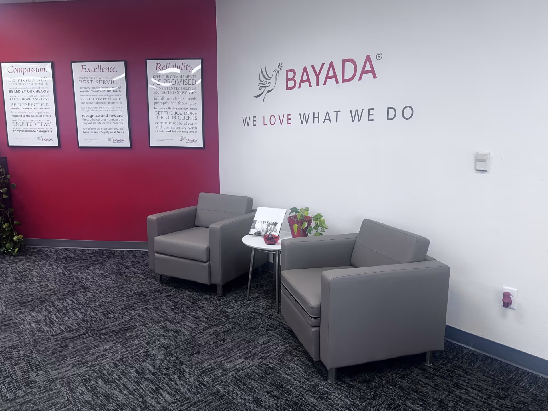 Lobby seating area with two gray armchairs, a small white table, and a BAYADA logo wall.