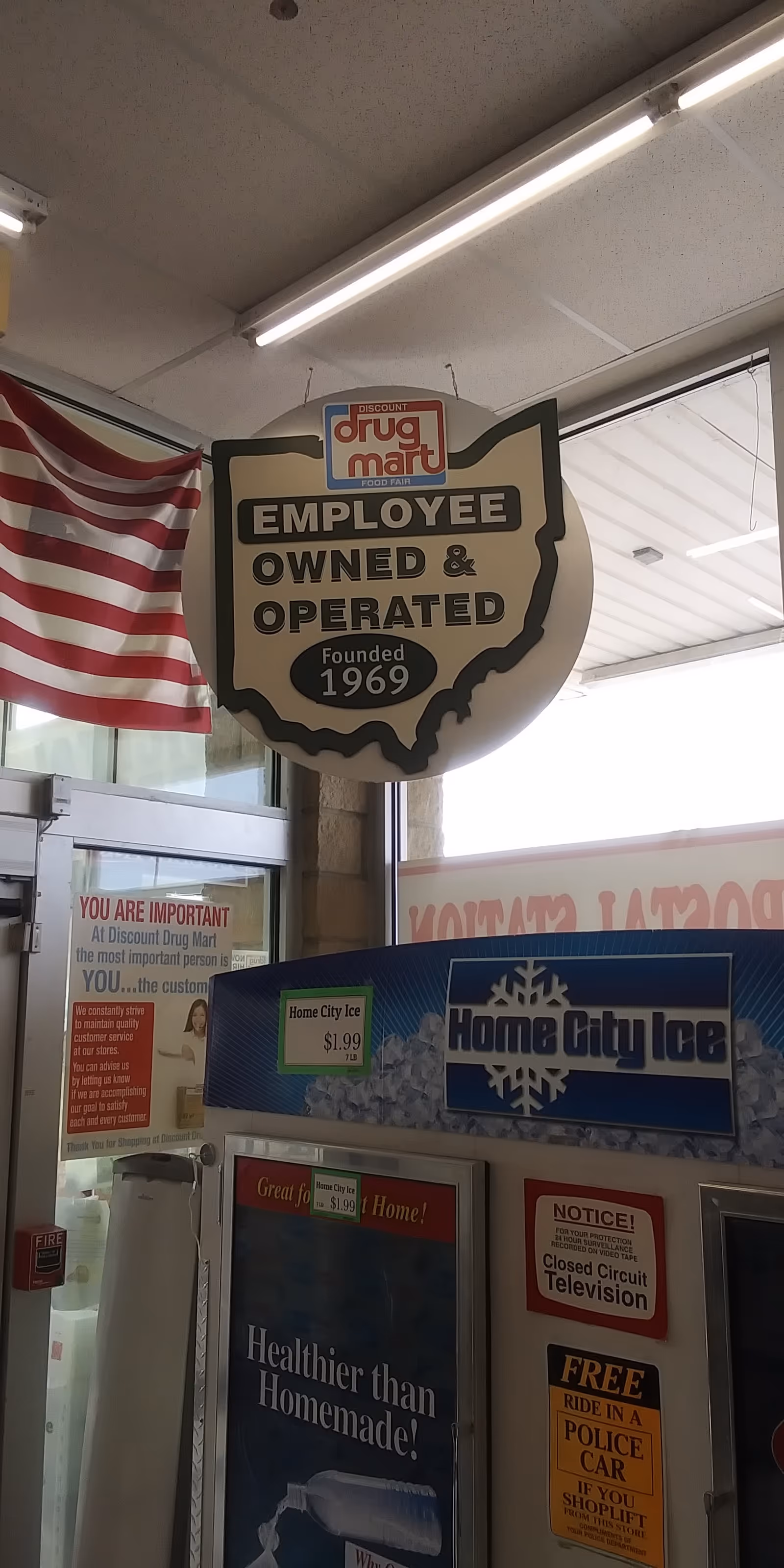 Discount Drug Mart employee-owned sign hanging inside a store, with an American flag nearby.