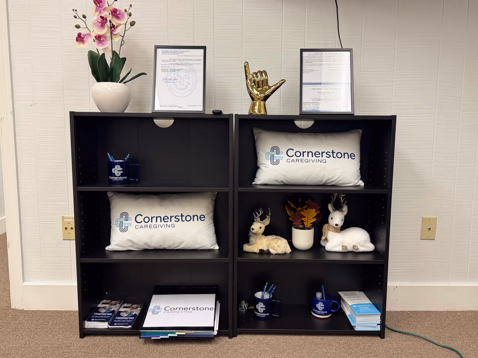 Interior lobby shelving with Cornerstone Caregiving pillows, framed certificates, and decorative reindeer figures.