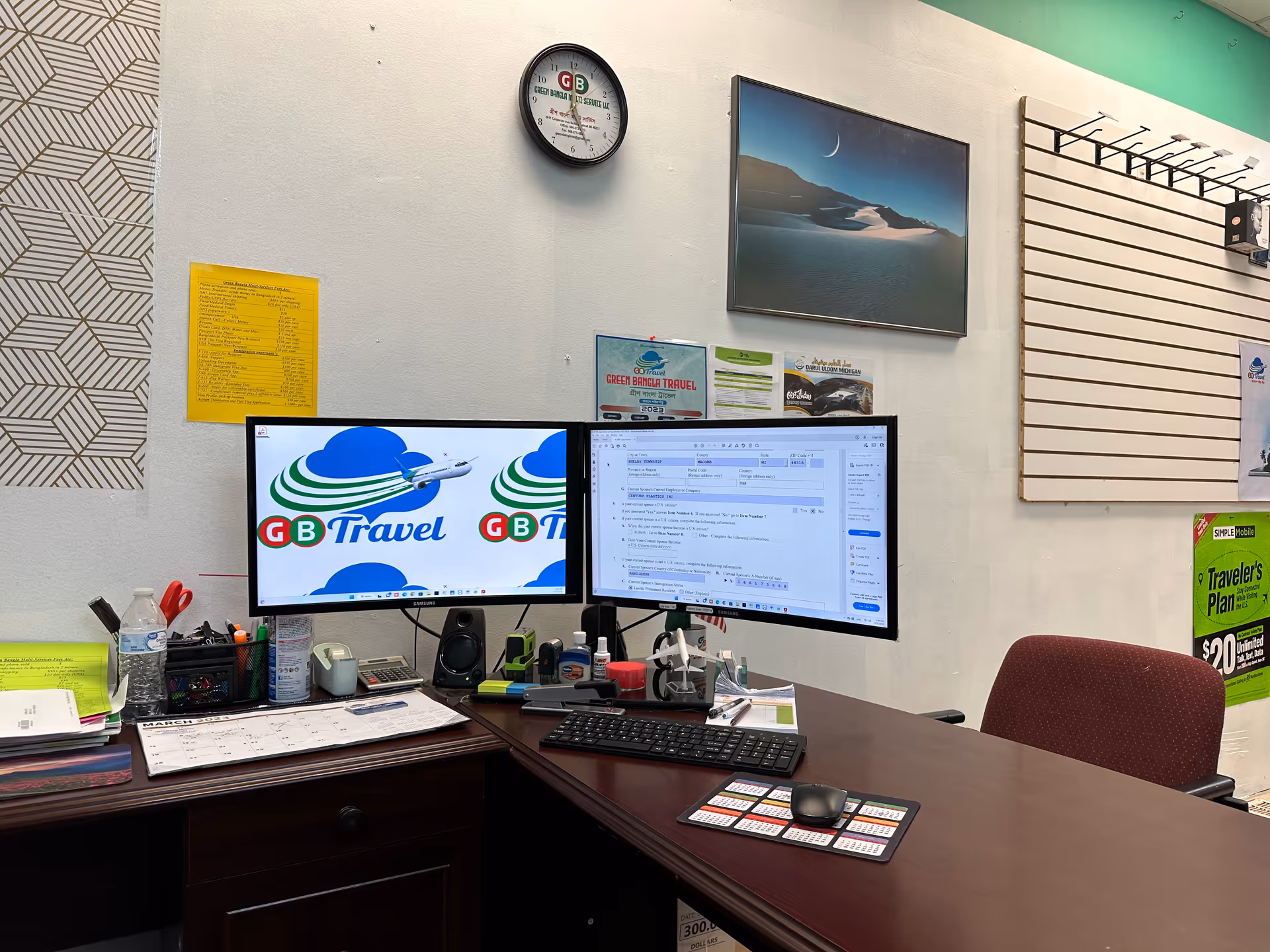 Office desk with dual monitors displaying travel branding and various office supplies.
