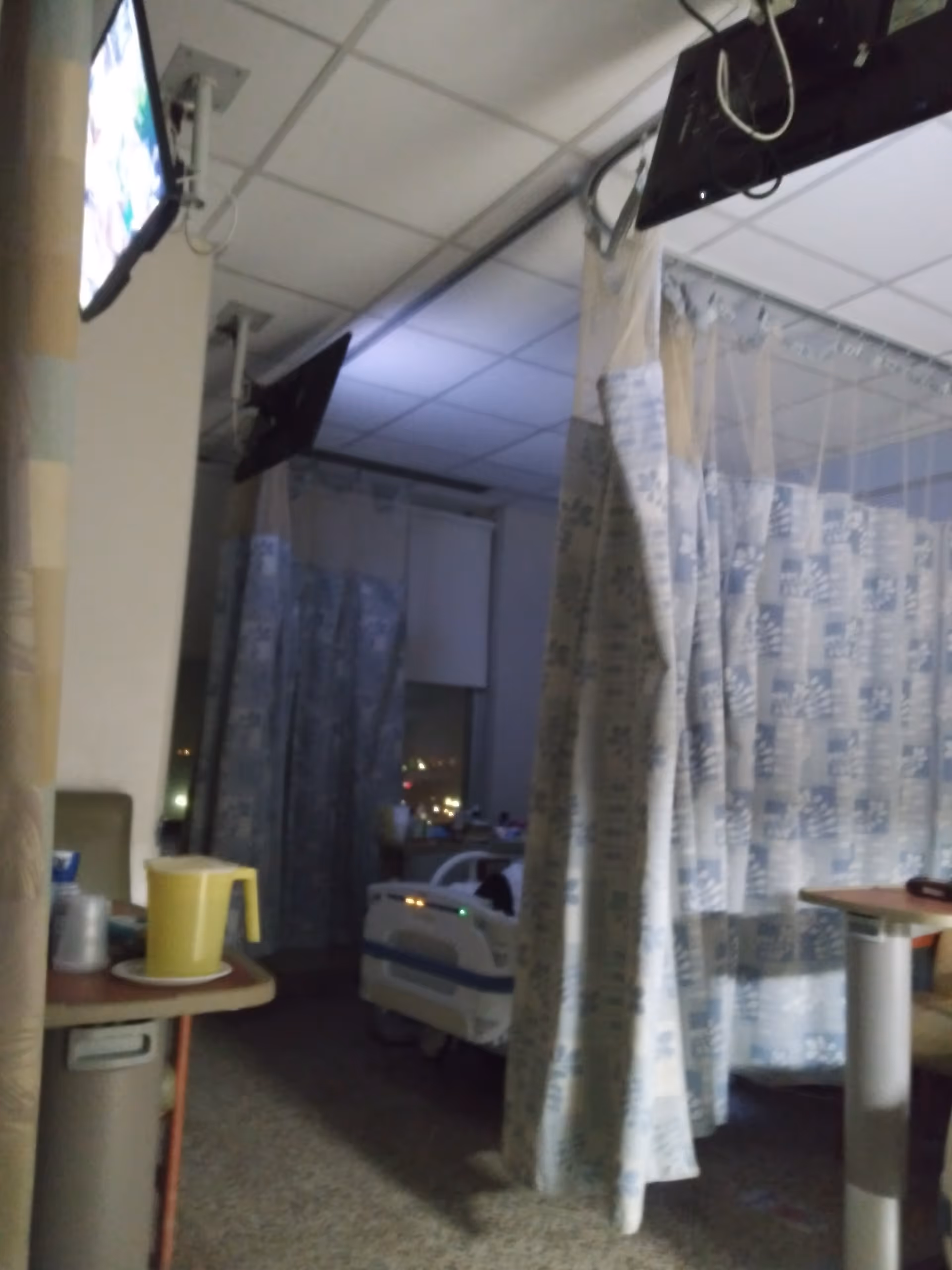 Hospital patient room with blue privacy curtains, a bed, and medical equipment visible.