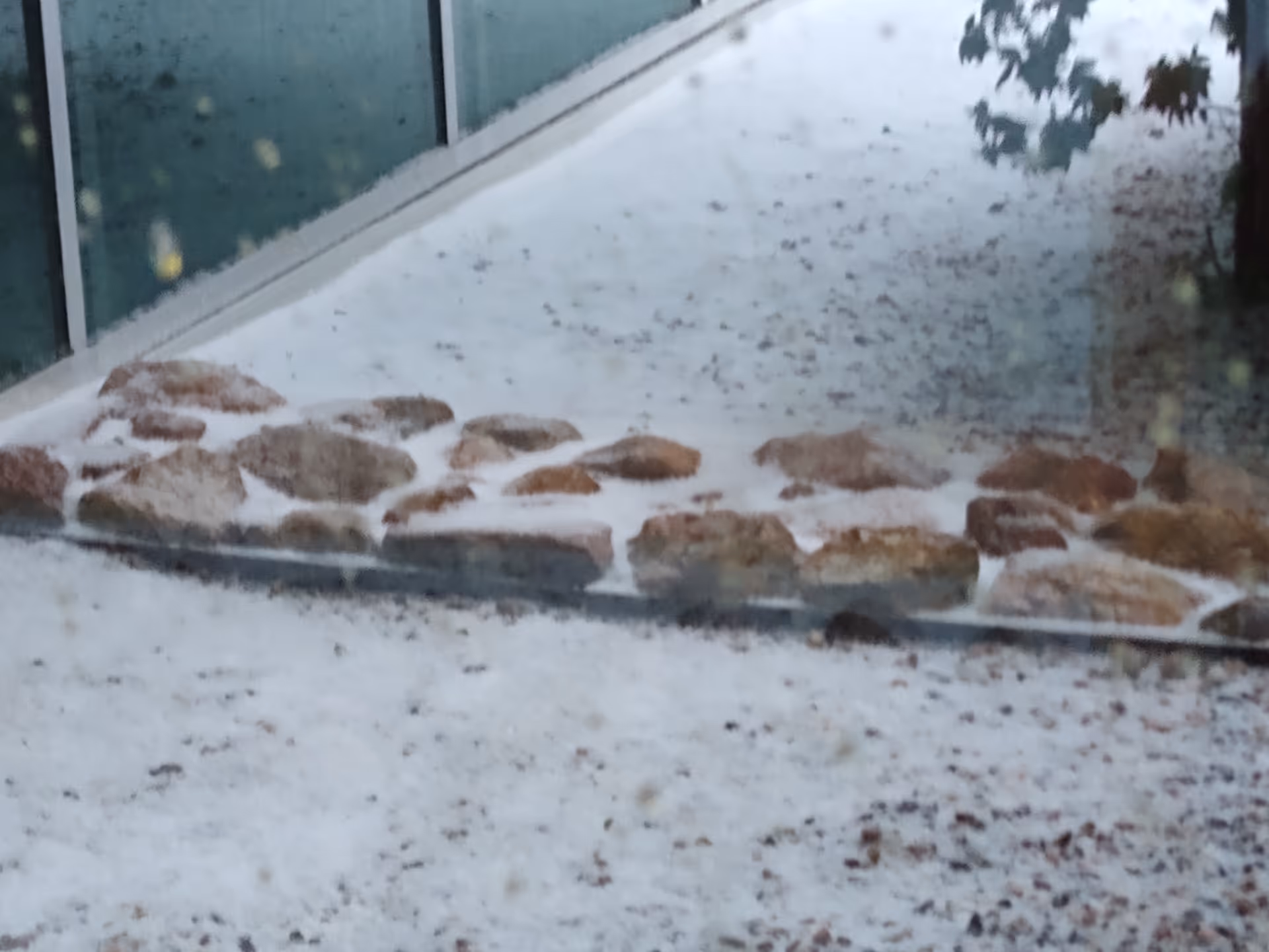 Snow-covered outdoor walkway beside a glass building with stone edging.