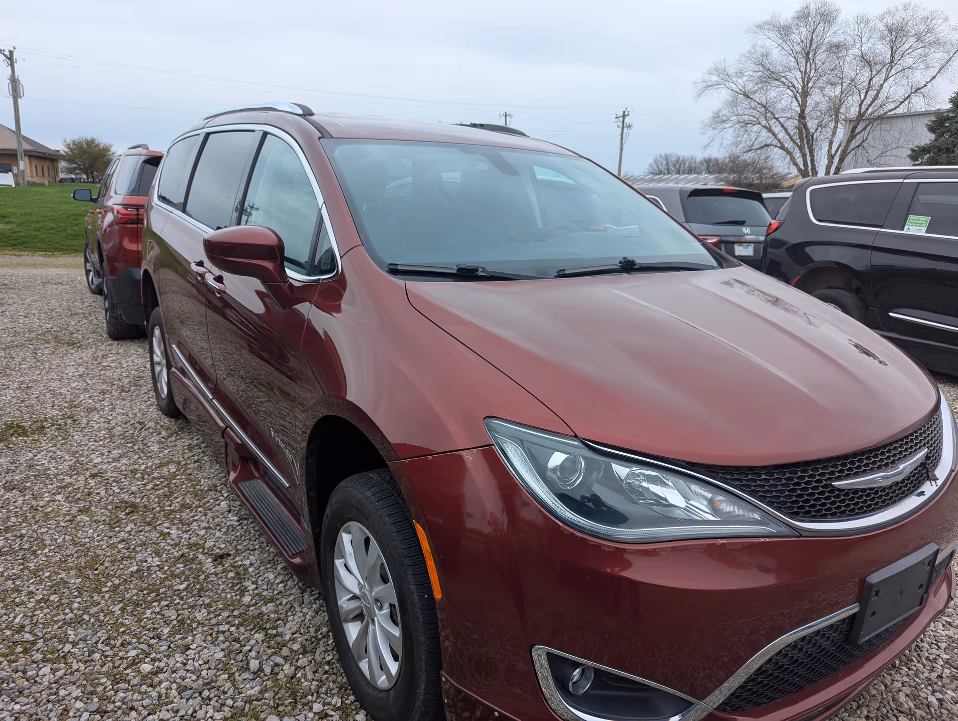 Maroon minivan parked on a gravel lot with other vehicles.