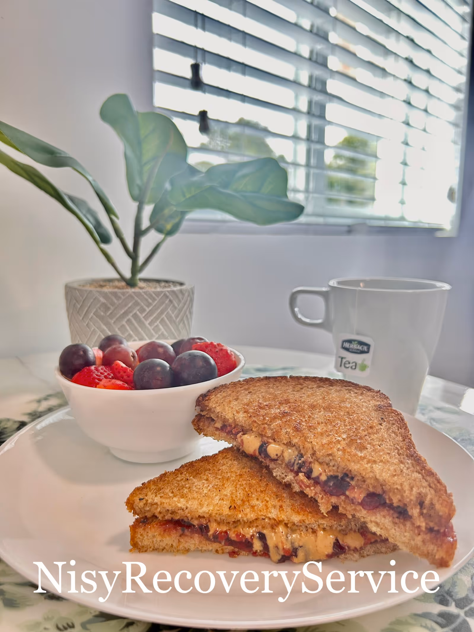 Plate with toasted sandwich, berry bowl, and mug of tea on a table by a window.