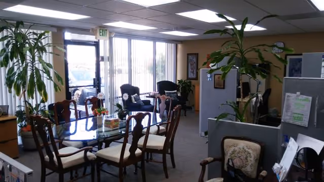Senior living dining area with glass table, chairs, and potted plants.