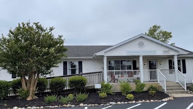 Single-story building with white siding, front porch, ramp, and landscaped front area.
