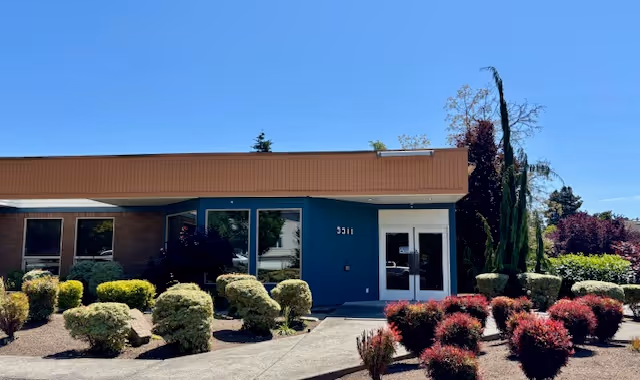 A single-story building exterior with a blue entrance and manicured landscaping.