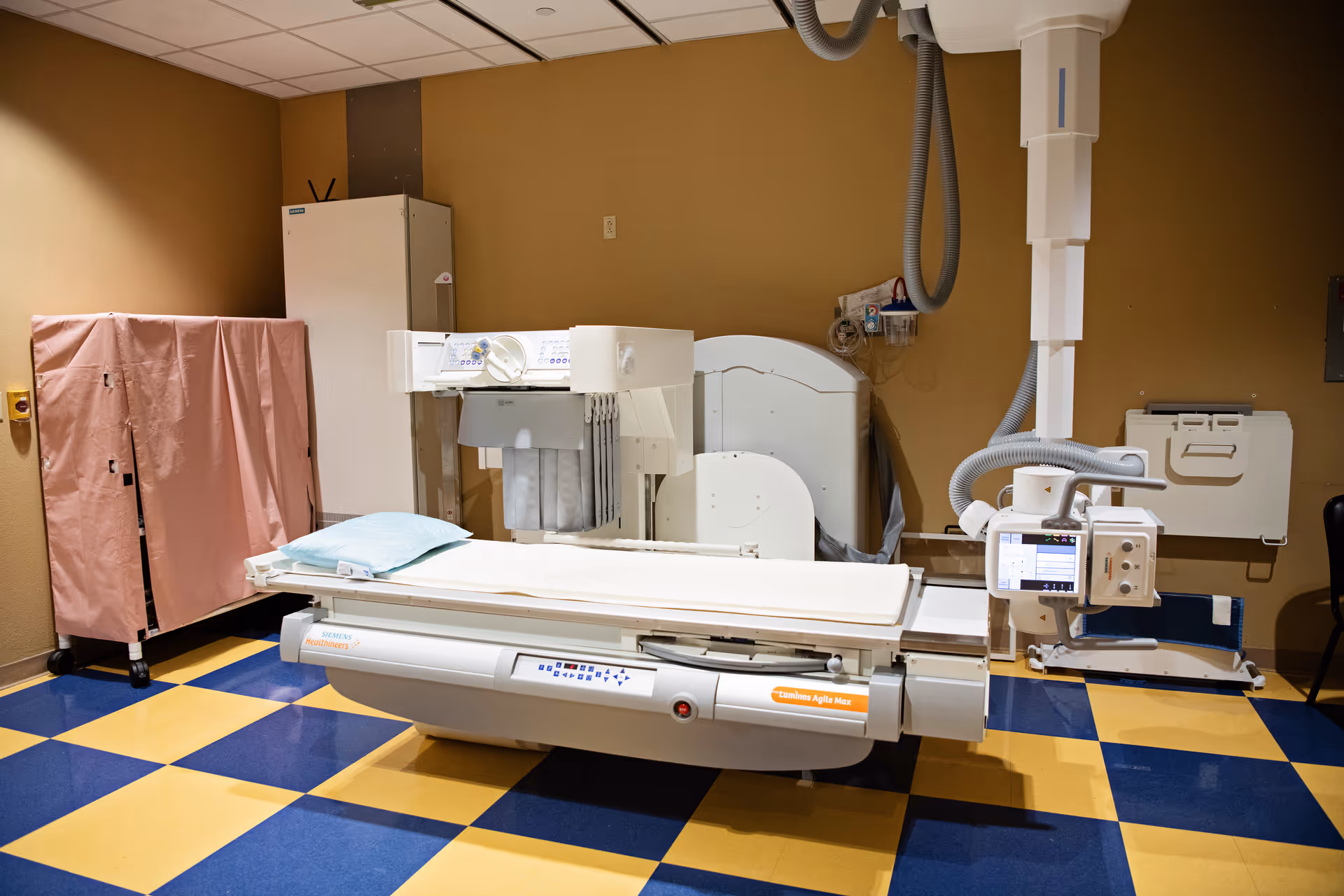 Medical imaging room showing a large bed scanner and blue-yellow checkered floor.