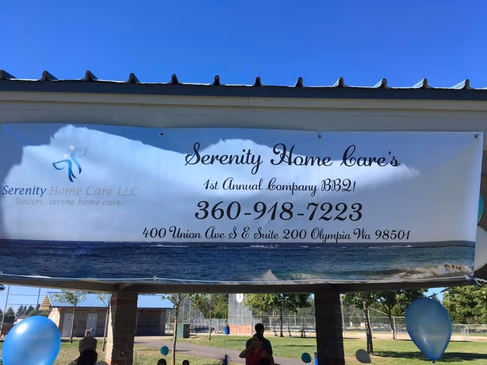 Outdoor banner advertising Serenity Home Care's BBQ event, attached to a pavilion under a blue sky.