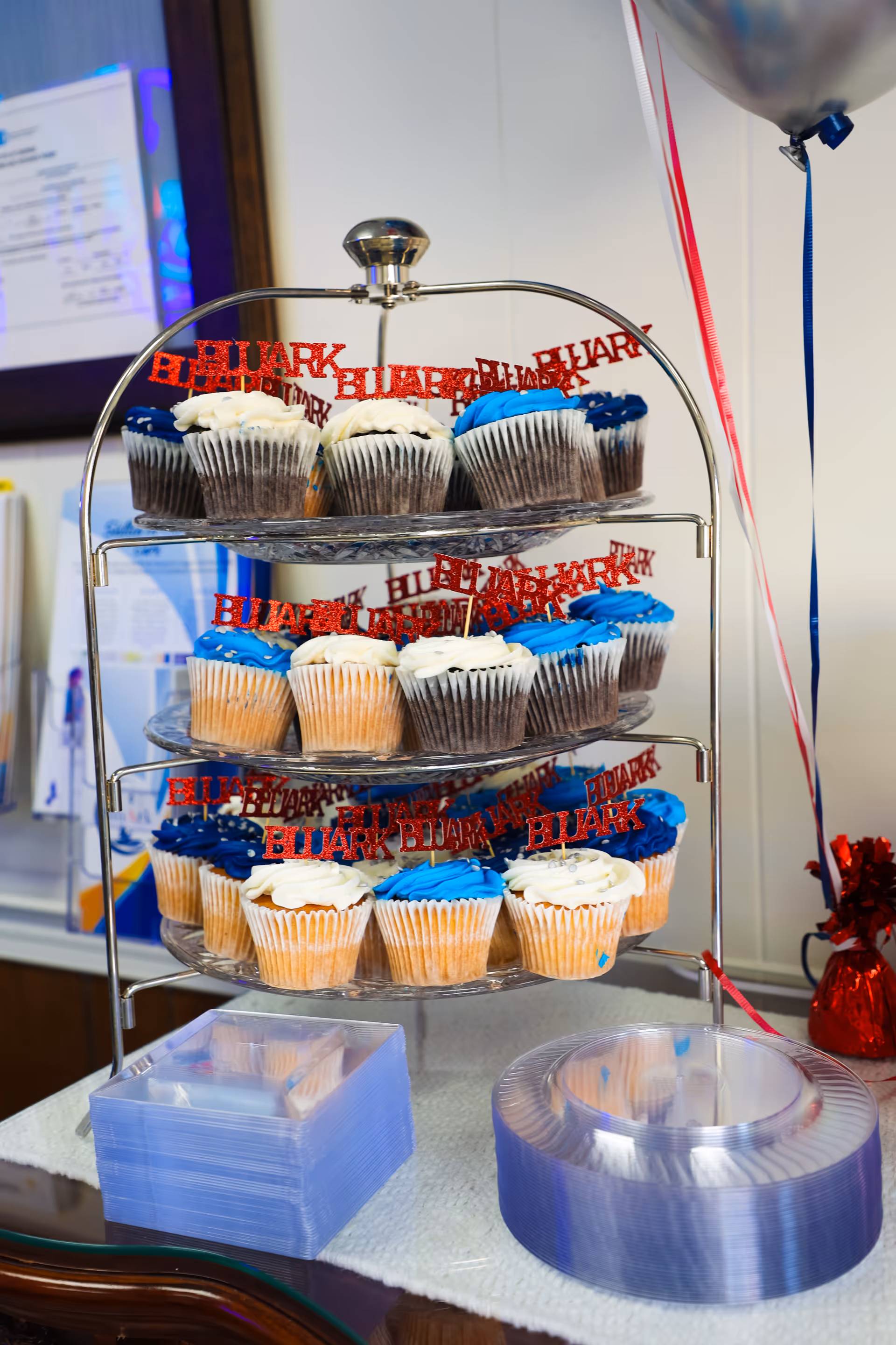 Tiered metal cupcake stand displaying blue and white frosted cupcakes indoors at BluArk