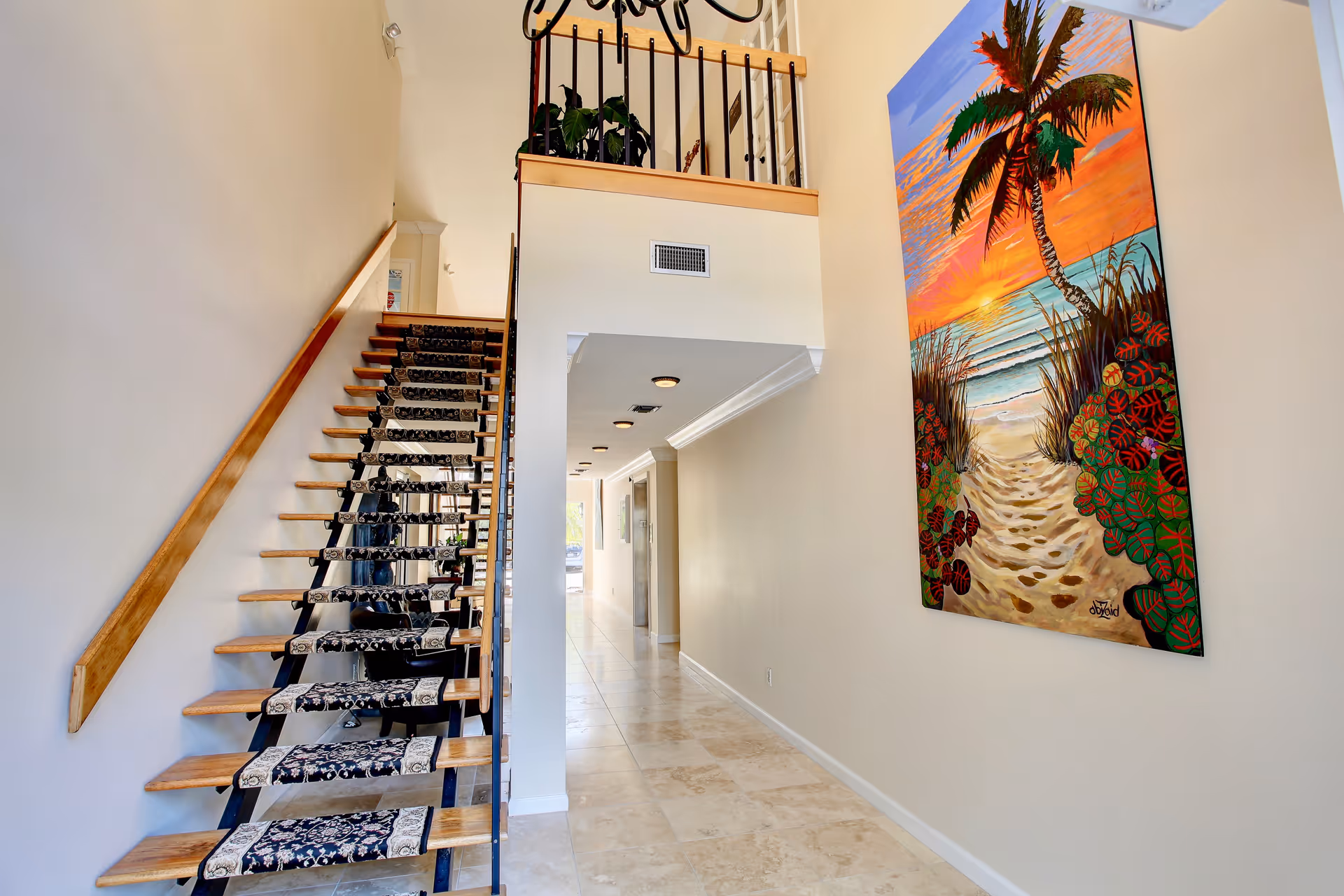 Interior hallway with a wooden staircase and a palm-themed painting on the wall.