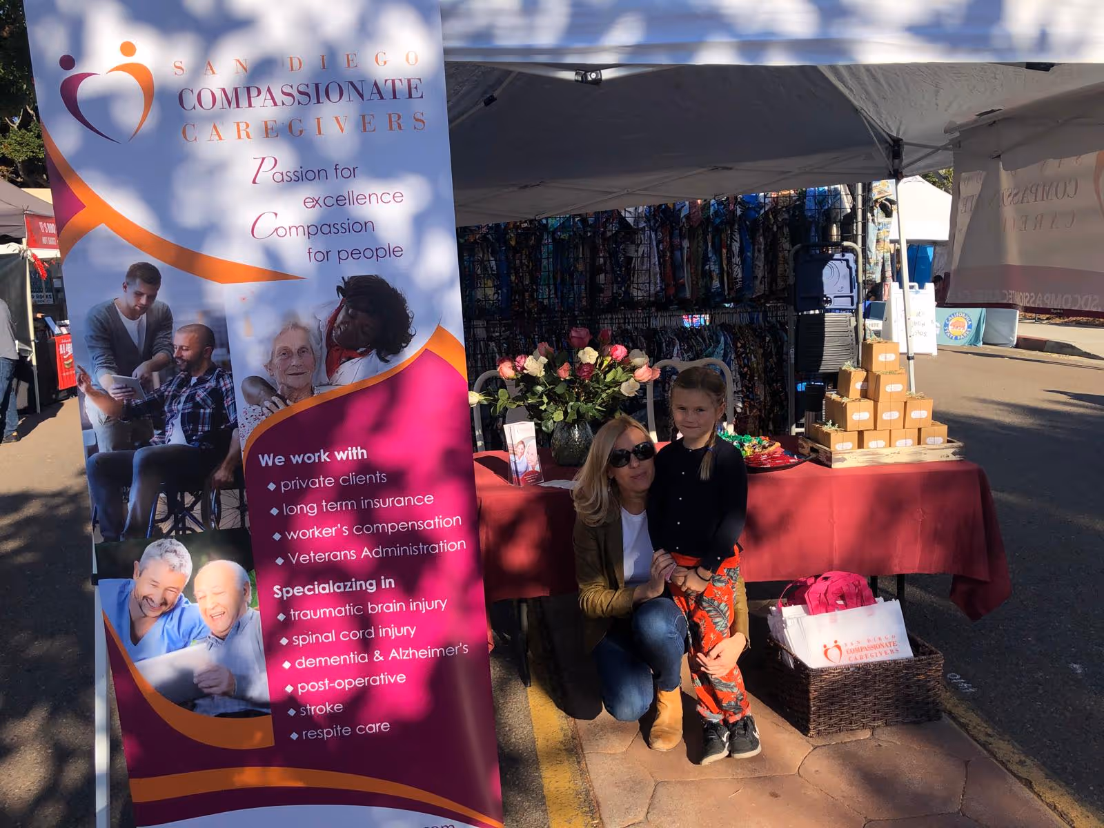 Woman and child pose beside a promotional booth under a large Compassionate Caregivers banner.