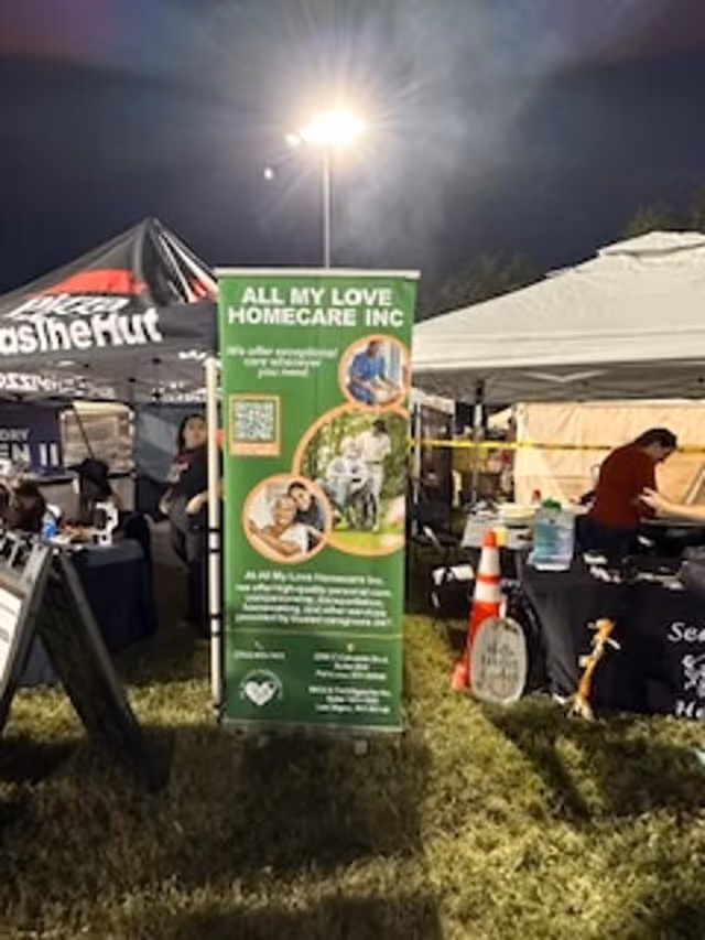 Outdoor booth setup with green All My Love Homecare banner at a nighttime event.