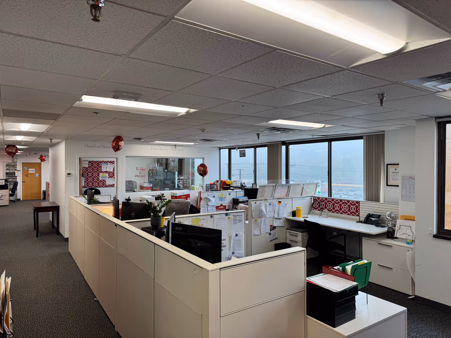 Open office area with cubicles, desks, papers, and large windows inside BAYADA facility.