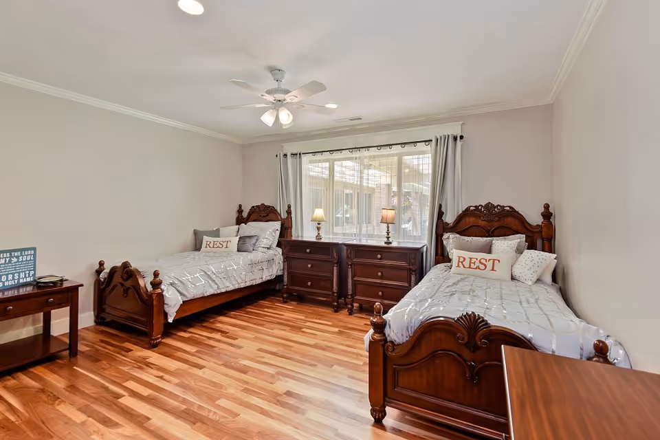 Two twin beds with ornate wooden frames flank a central dresser by a window.