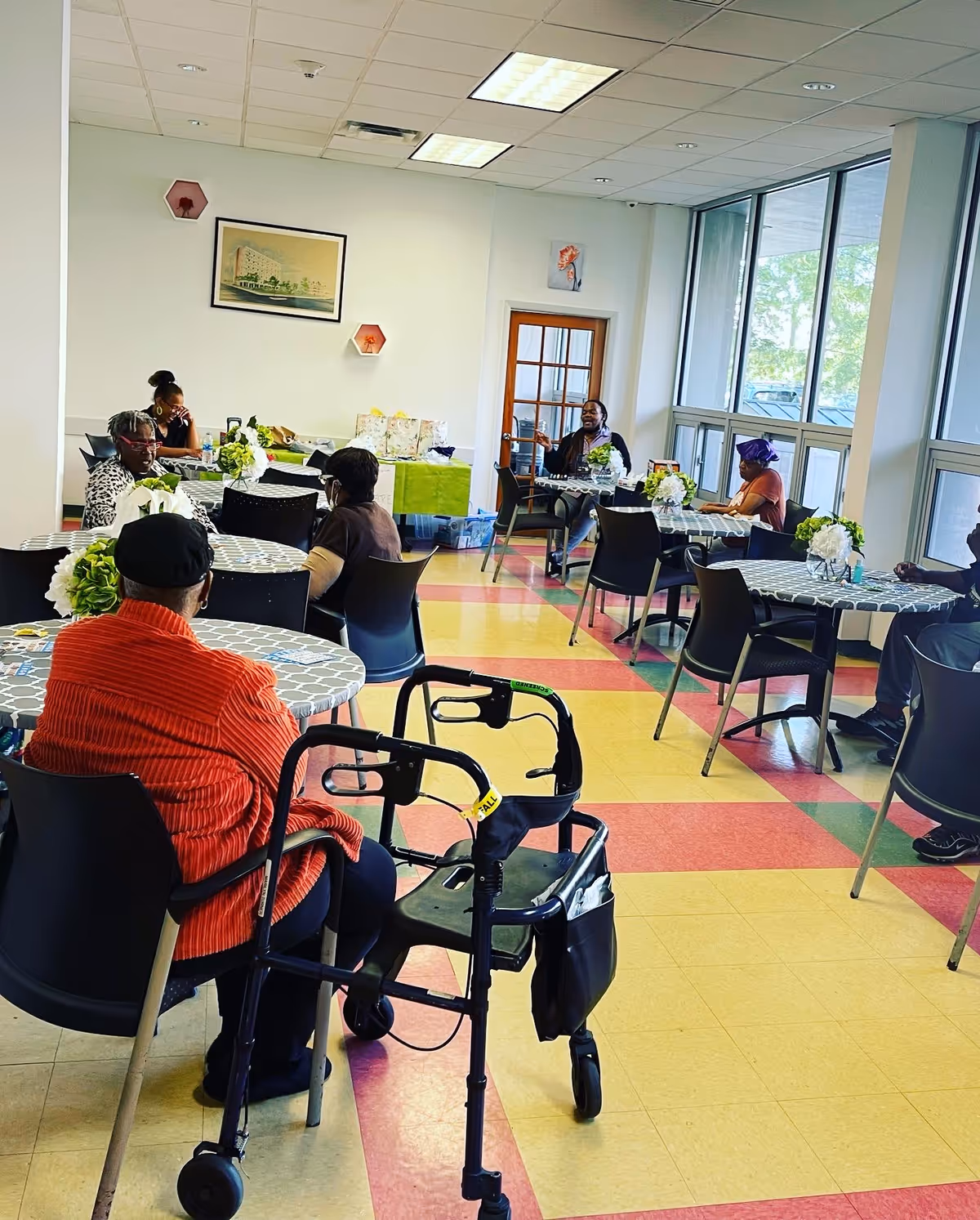 Residents sit at round tables with flower centerpieces in a bright dining room.