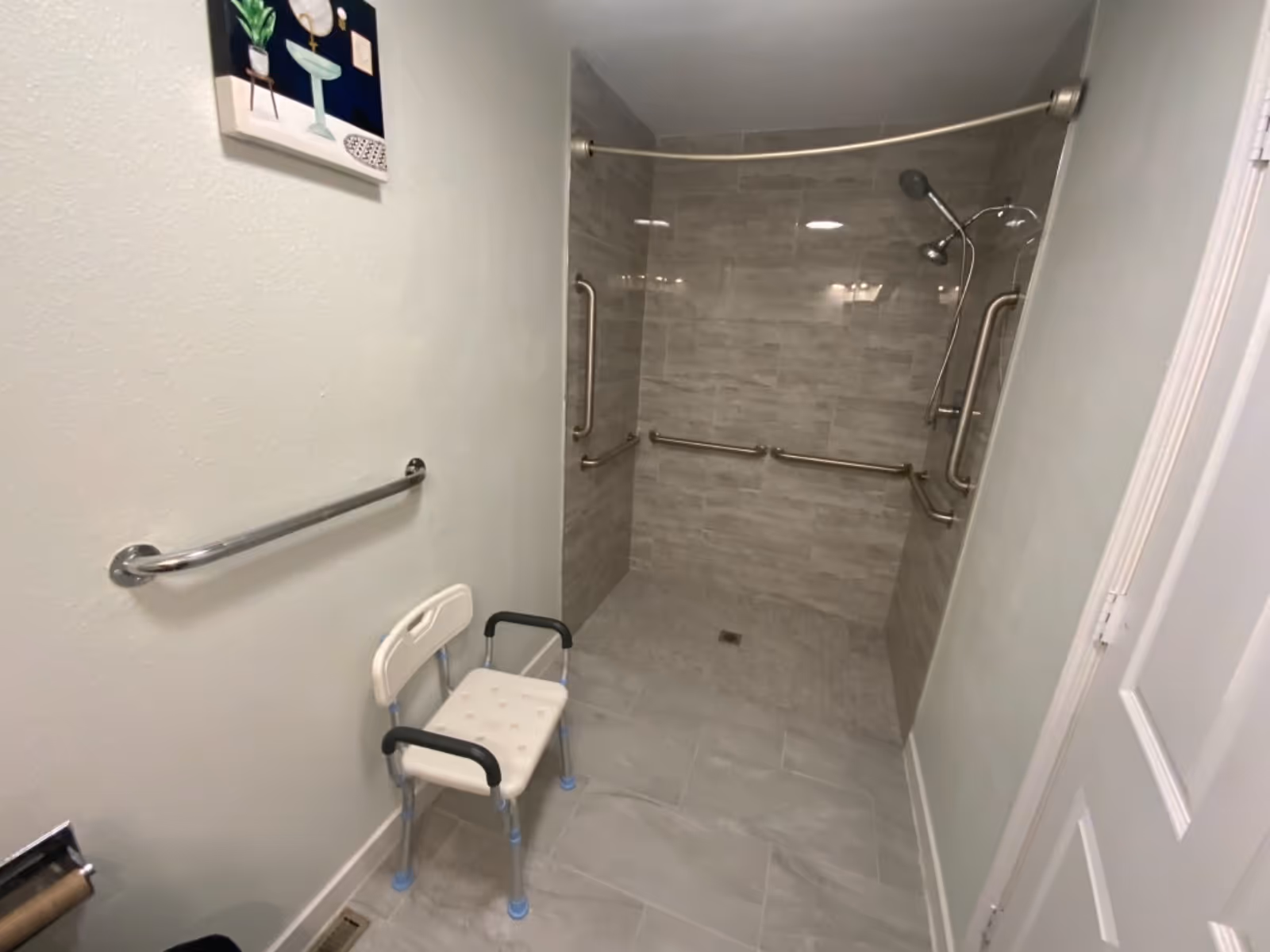 Accessible tiled shower area with grab bars and a small chair in a bathroom.