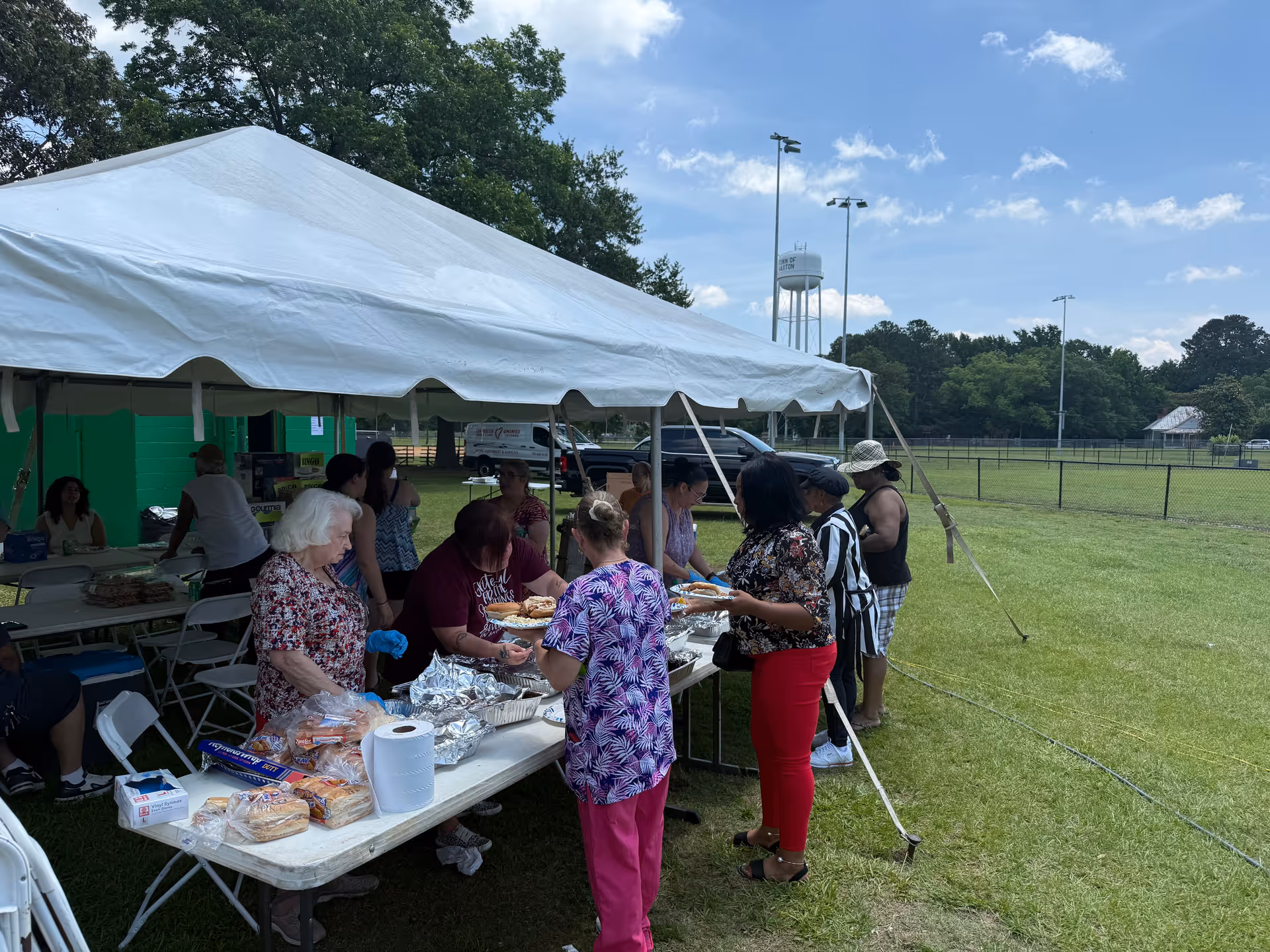 Outdoor event under a white tent with people serving and eating food.