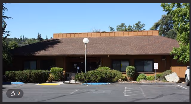 Front exterior of a single-story brown facility with shrubs and a parking lot.