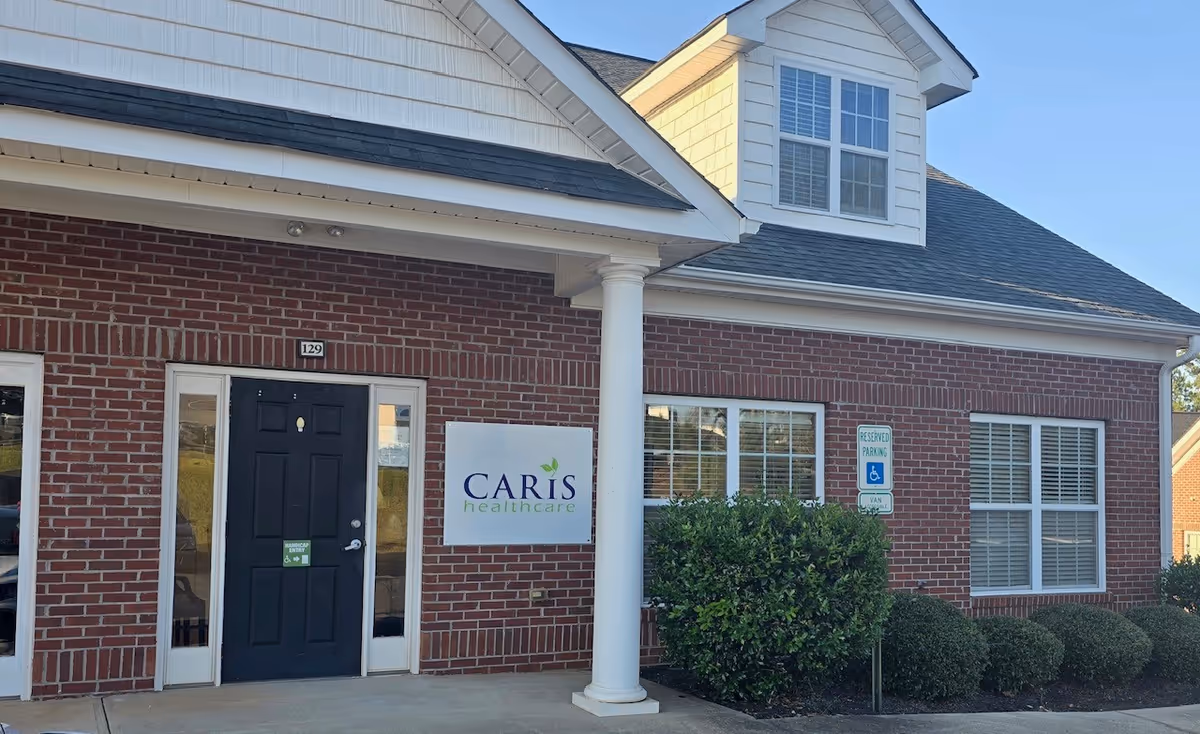Exterior view of a Caris Healthcare facility with front entrance, sign, and trimmed shrubs.