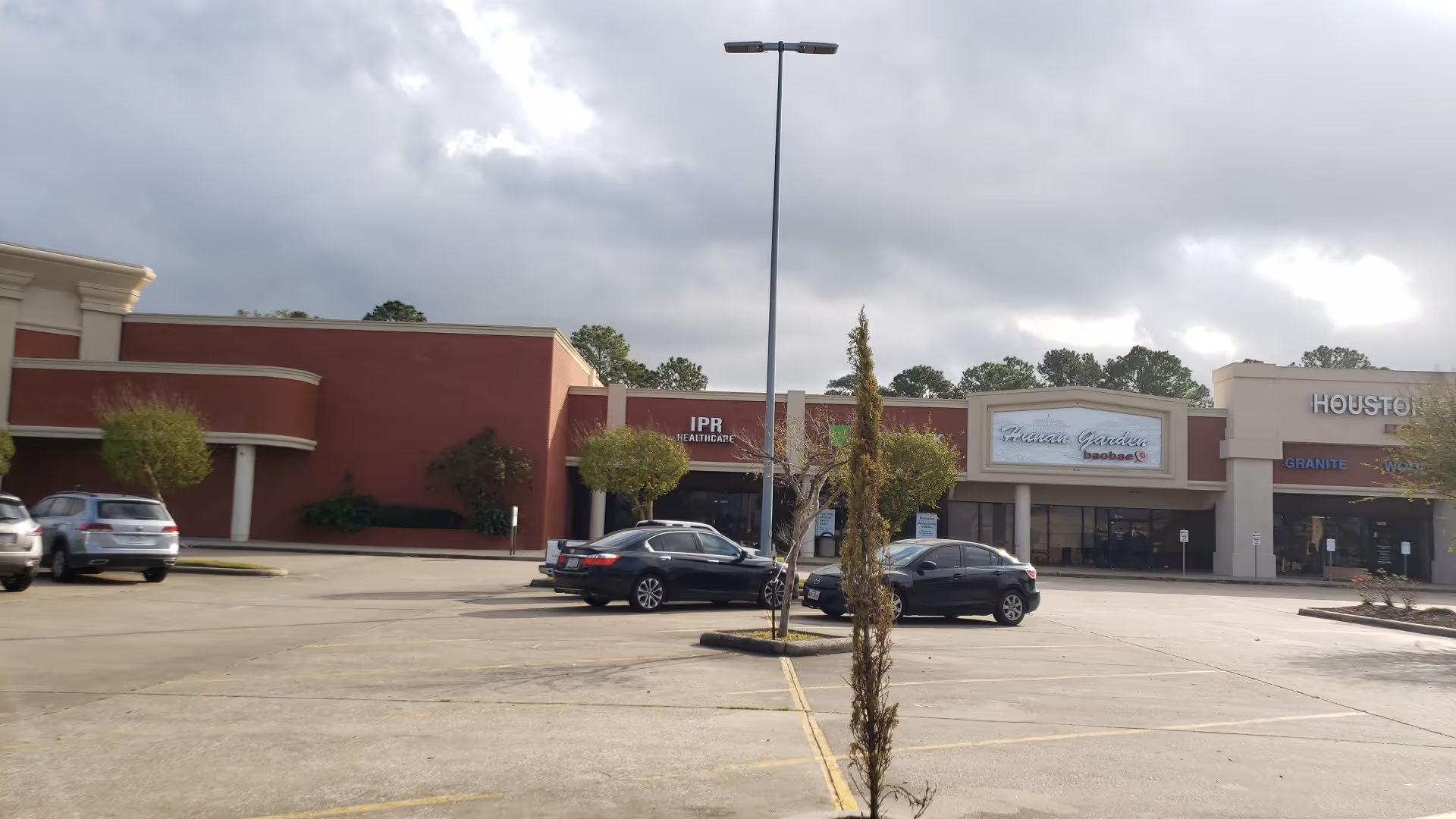 Exterior view of a strip mall with IPR Healthcare and other storefronts in a parking lot.