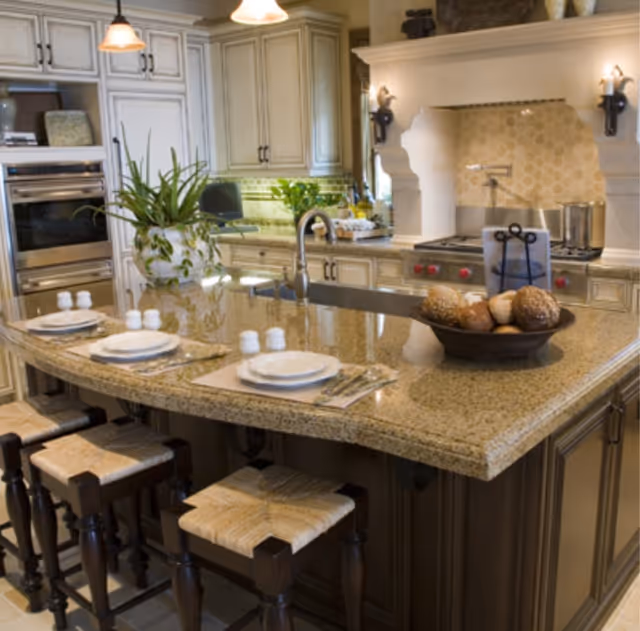 Polished kitchen in a senior living facility with granite island, stools, and built-in appliances.
