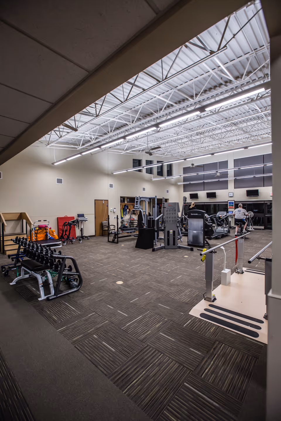 A gym inside a senior living facility with workout equipment and residents exercising