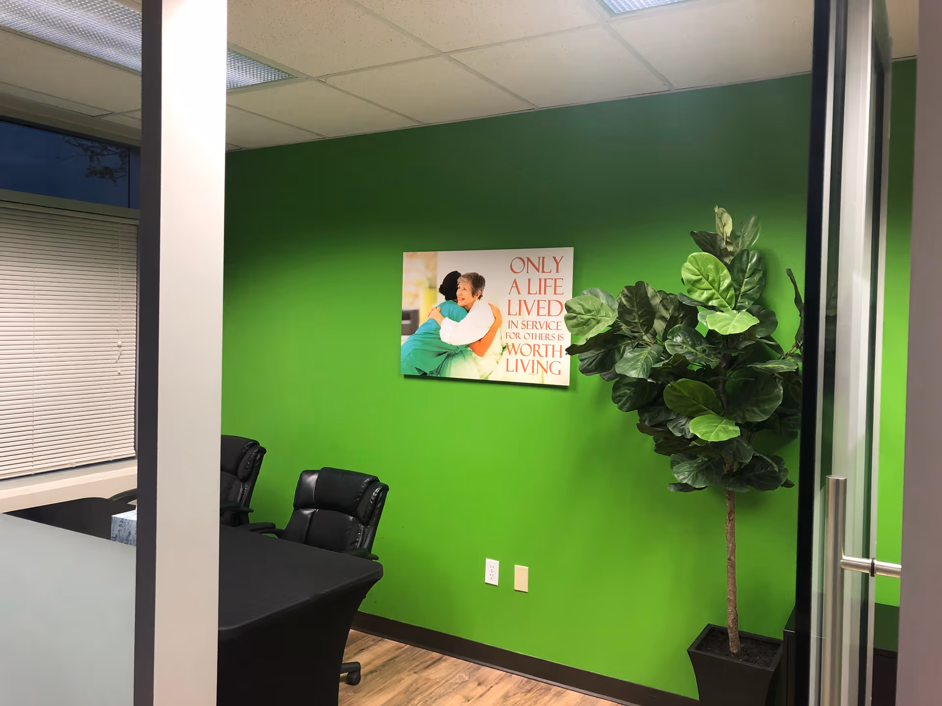 Bright green-walled meeting room with black chairs, potted plant, wall art near glass door.