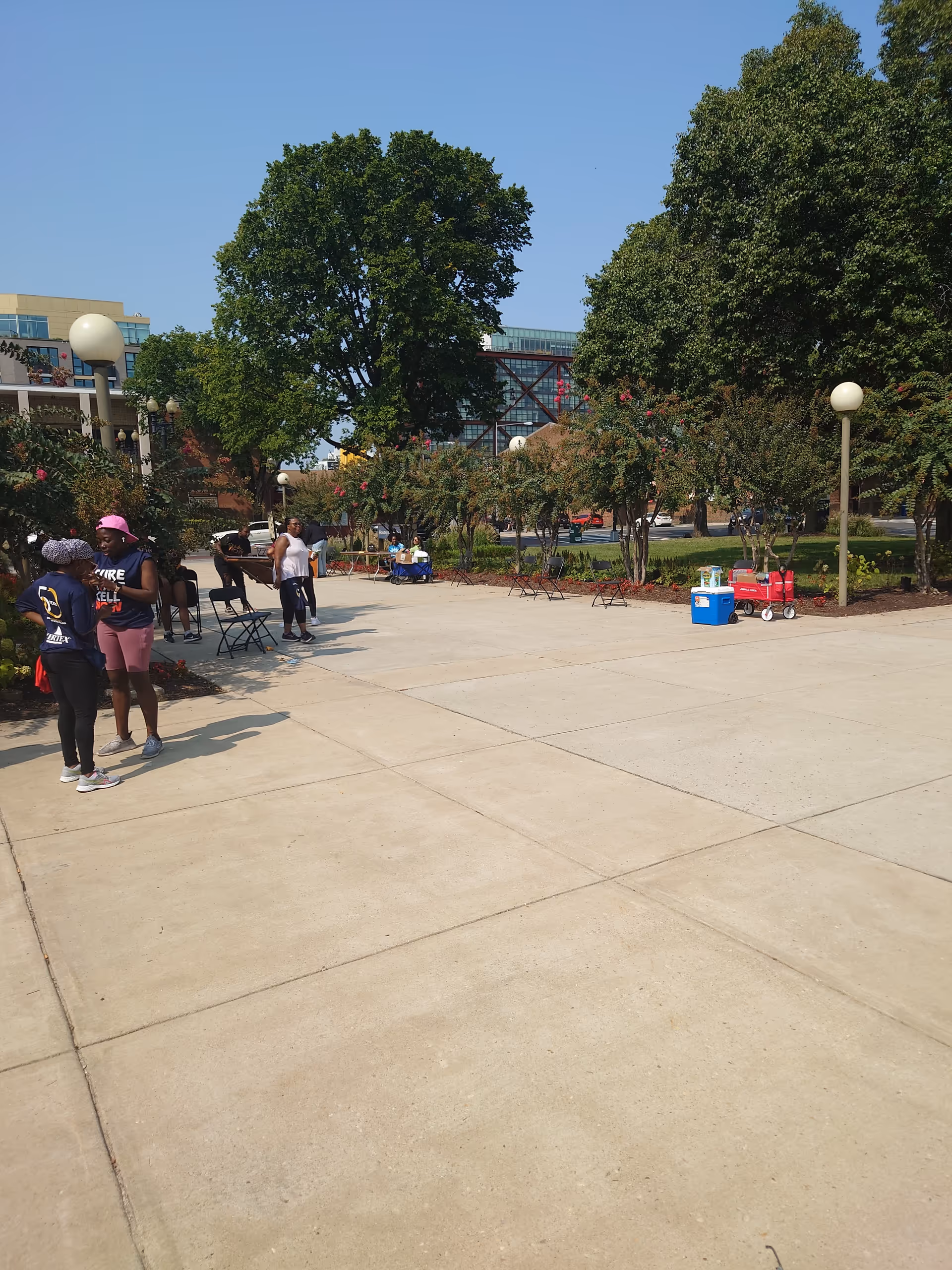Outdoor courtyard with trees, benches, and people gathered around seating areas.