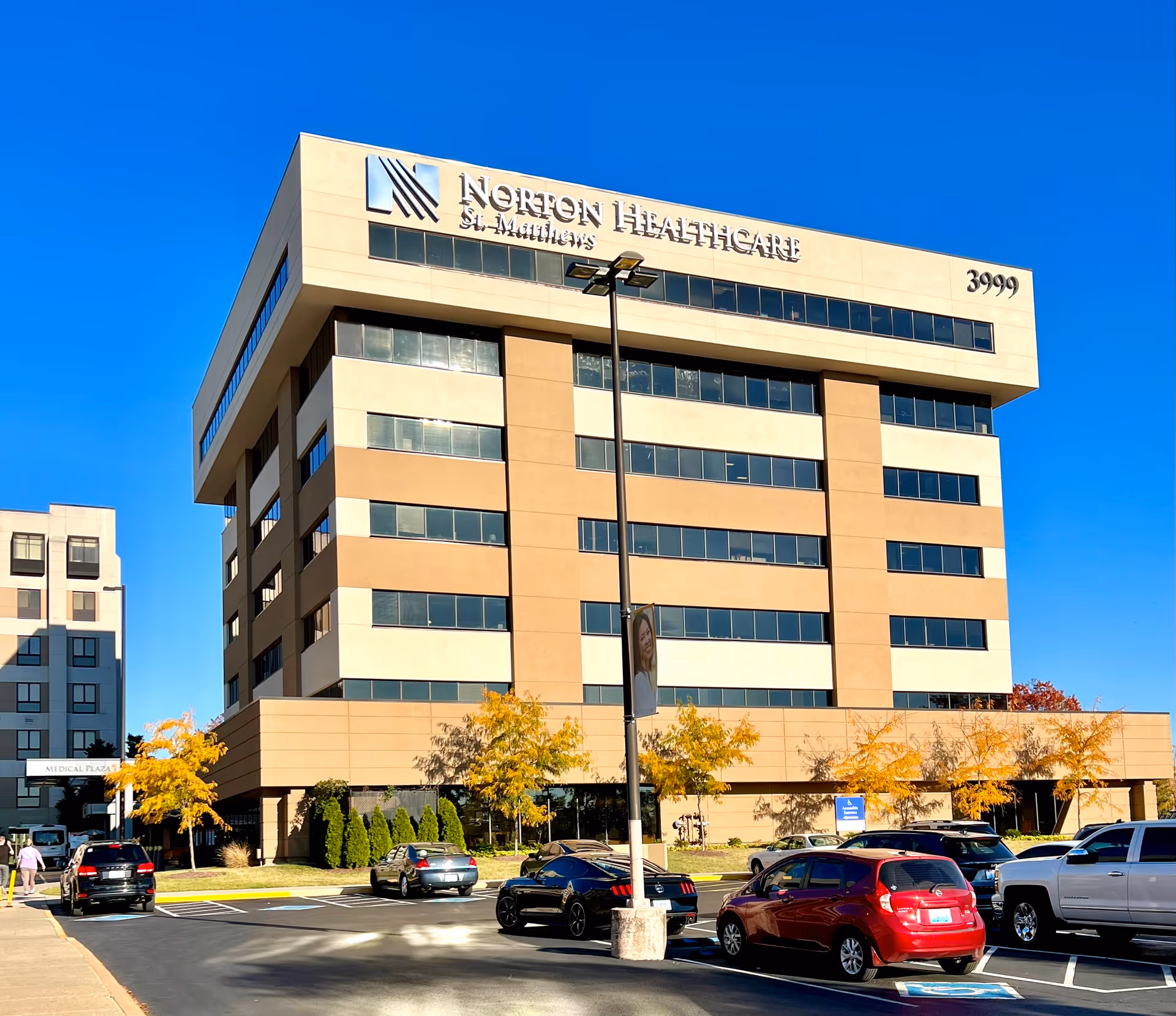 Modern multi-story Norton Healthcare medical plaza exterior with a parking lot and blue sky.
