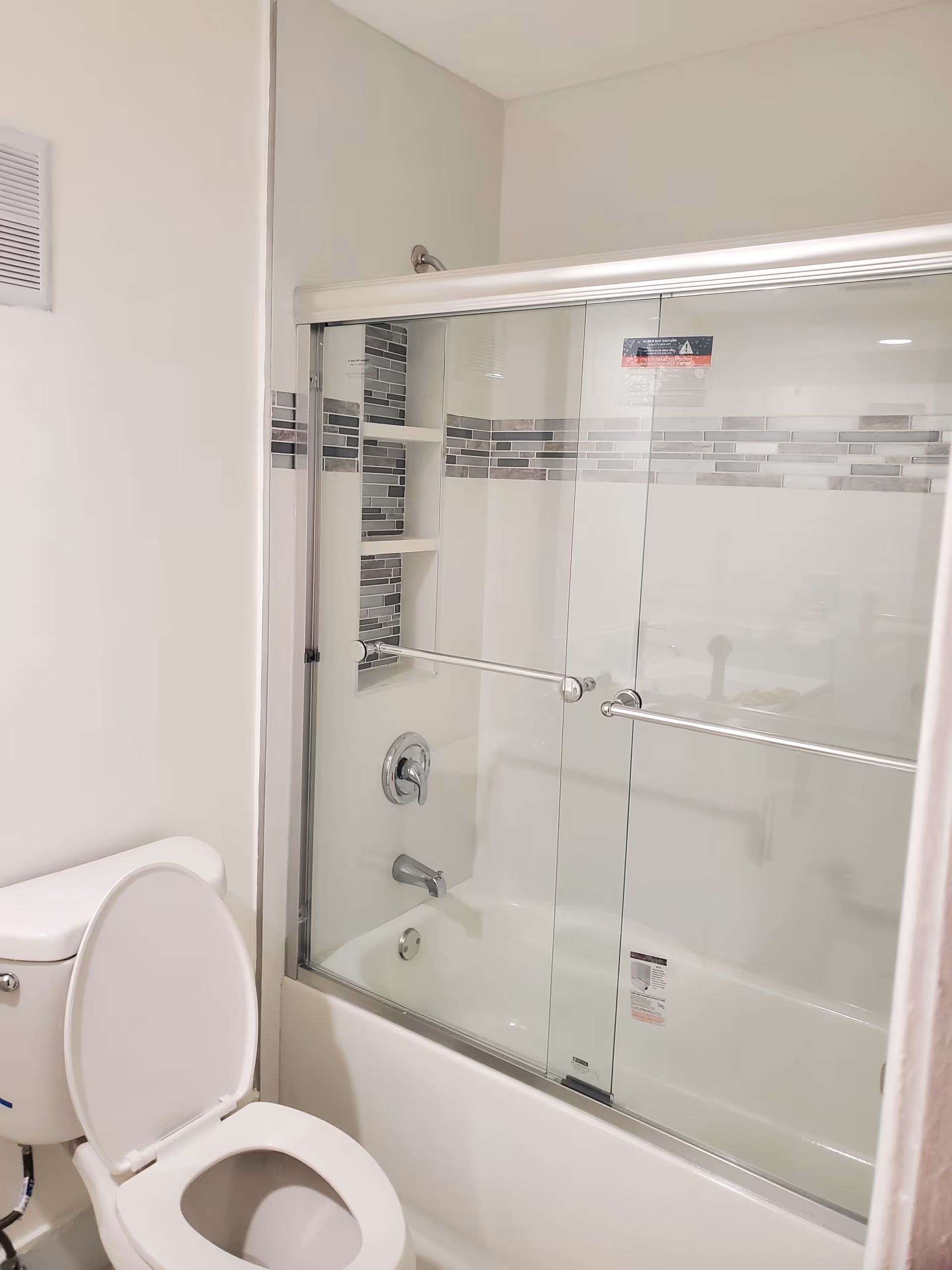 Modern bathroom with glass shower door, tiled wall, and toilet.
